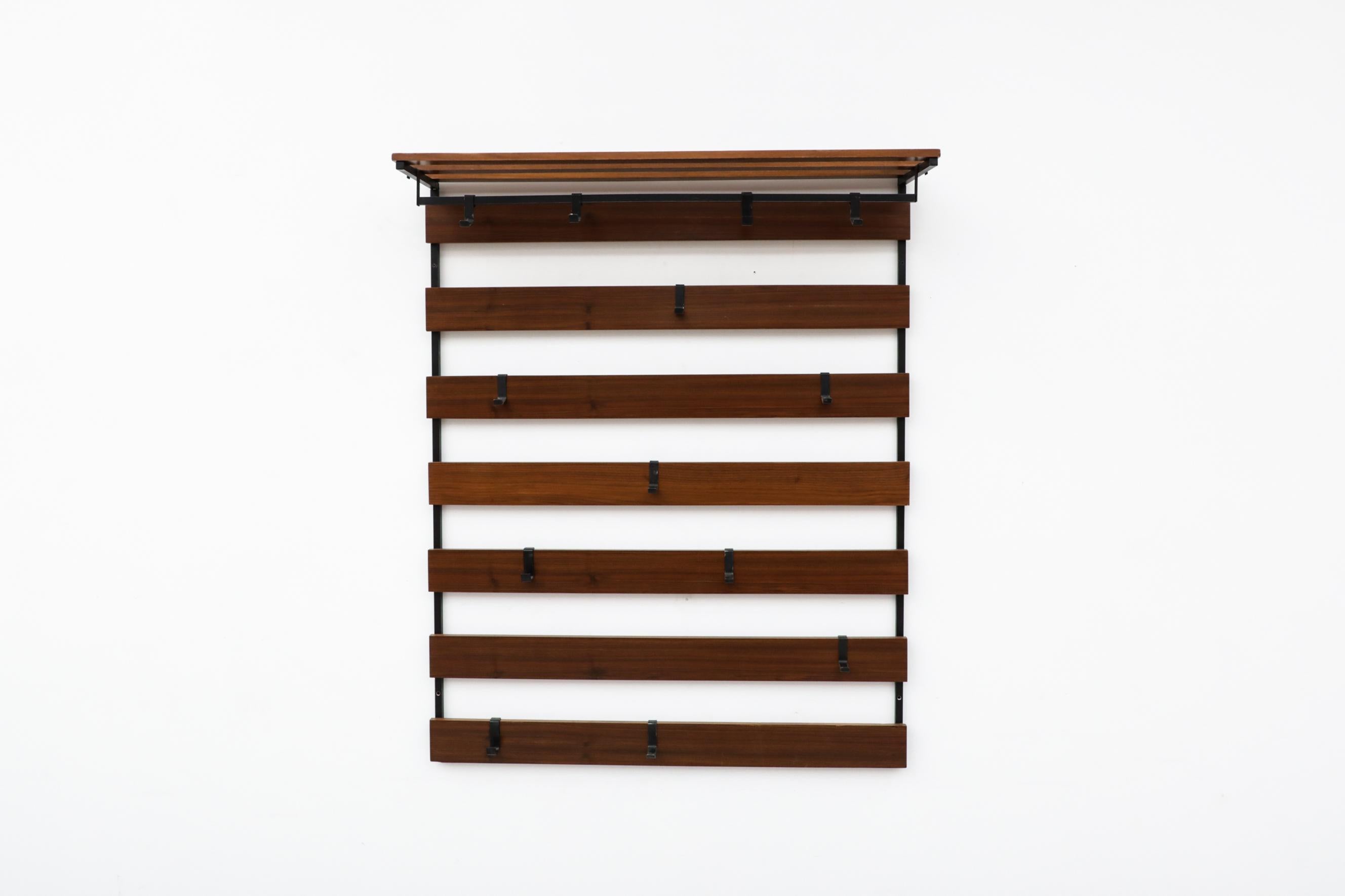 Midcentury teak slatted wall mount coat rack with hat shelf and 13 black moveable hooks. In original condition with visible wear and patina including some enamel loss. Wear is consistent with its age and use. Other wall-mounted coat racks are