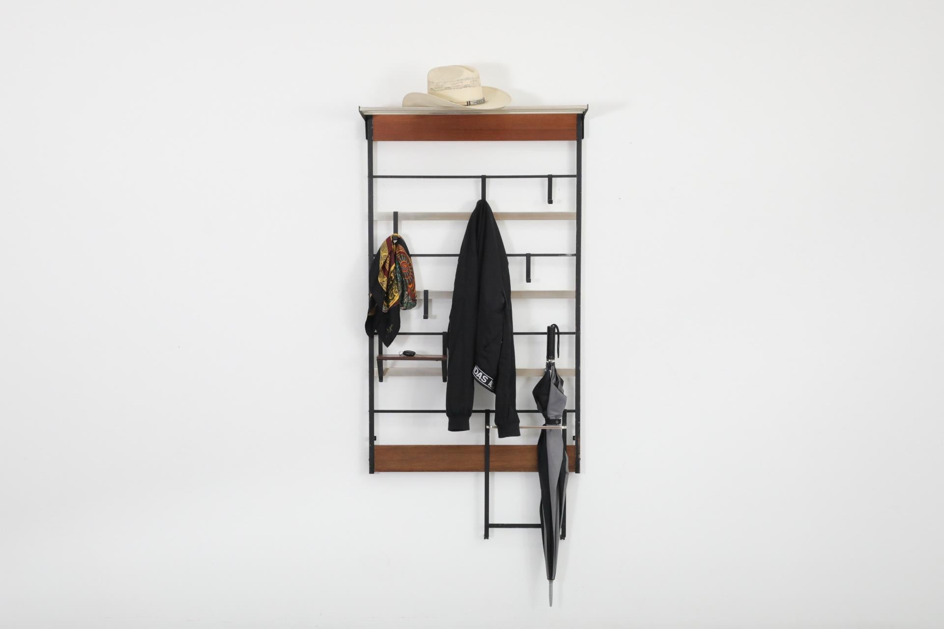 Perchero de pared de listones de teca y metal de mediados de siglo, con ganchos de alambre doblado de metal esmaltado en negro. Esta bonita pieza también tiene unos cuantos componentes móviles: un perchero, un estante de teca más pequeño y una barra
