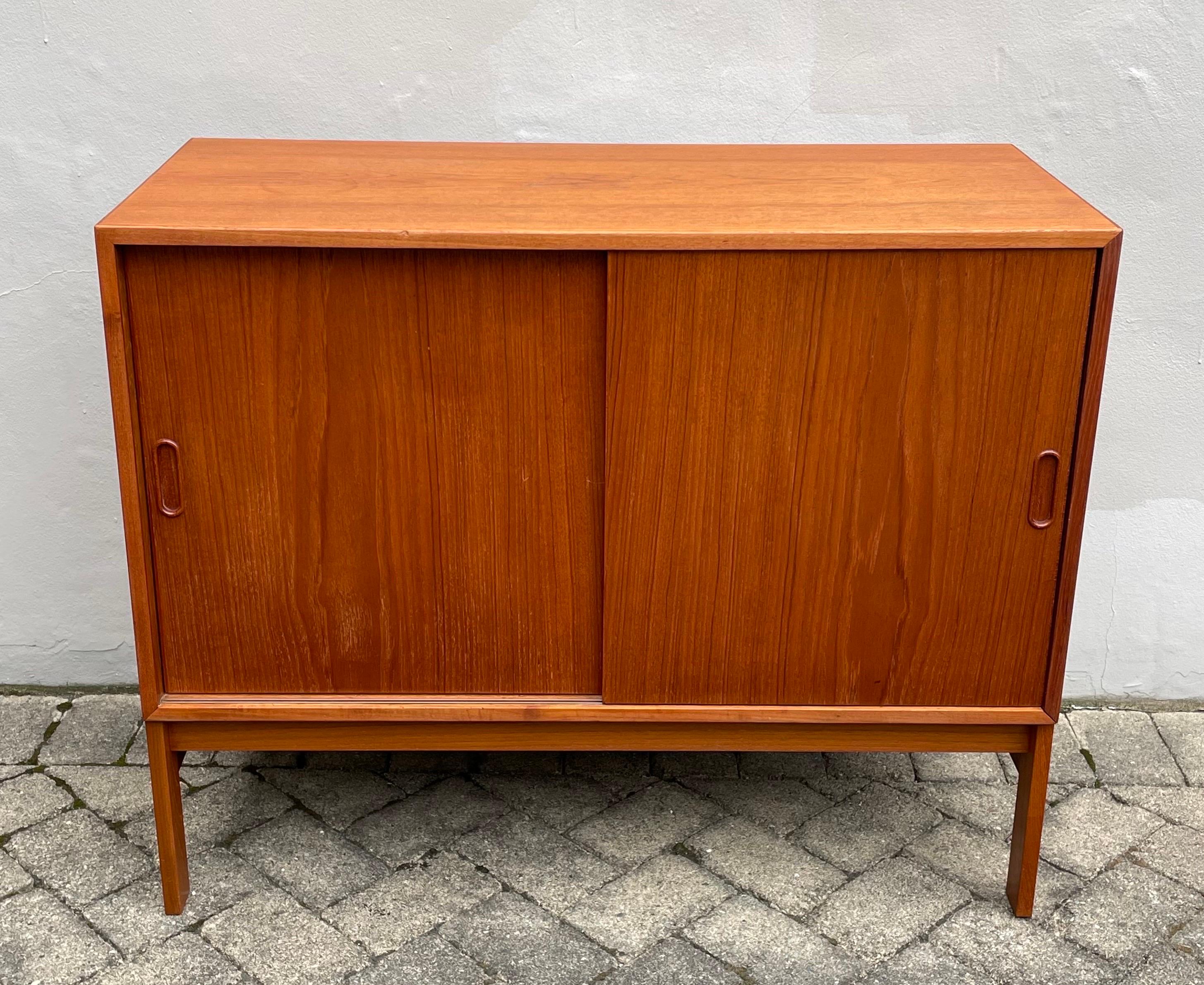 Authentic midcentury teak cabinet or small credenza by HG Furniture, Denmark. Two sliding doors with adjustable shelves. Beautiful condition with very minor surface scratches, minor repair on back leg, minor separation at one corner, please see all
