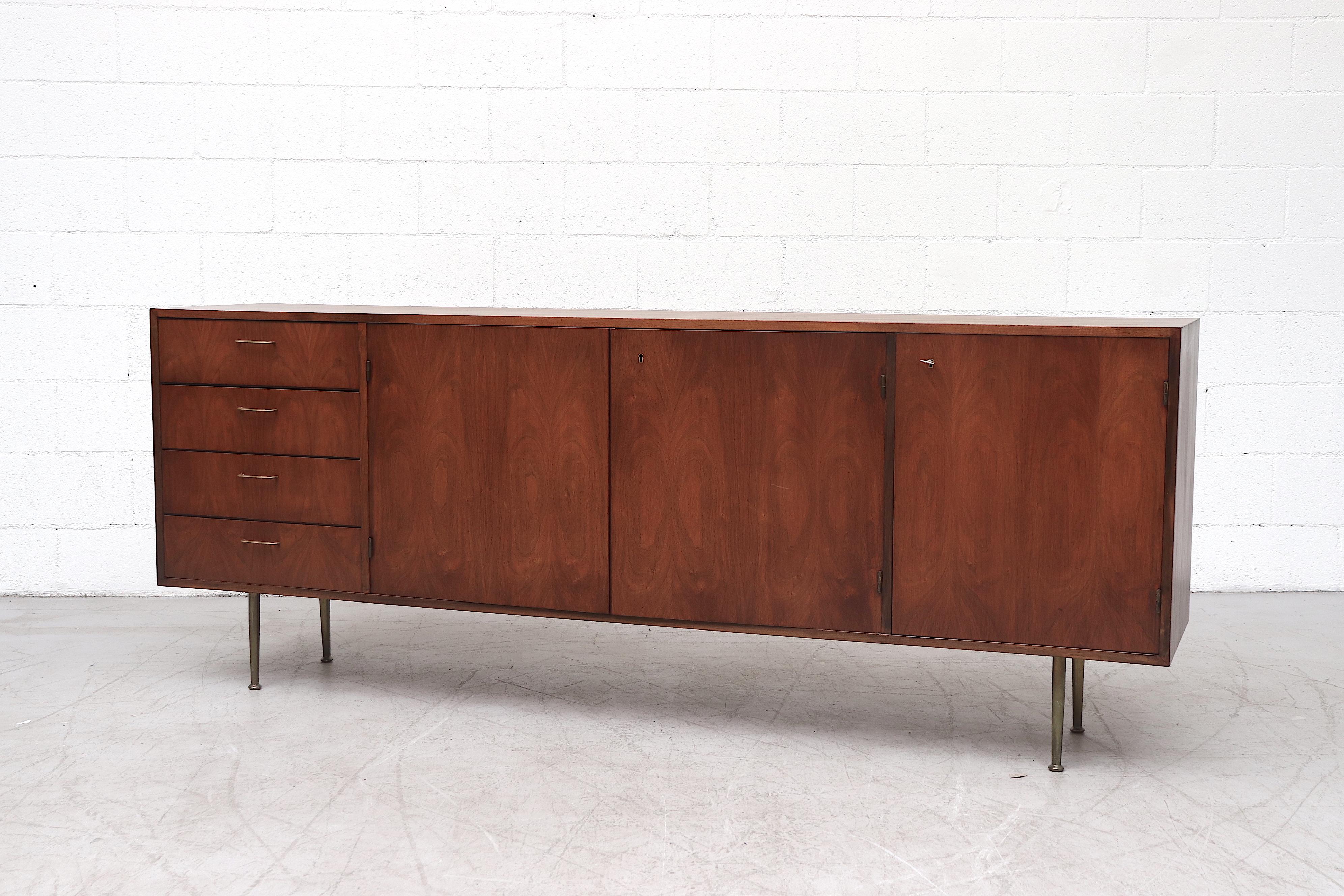 Beautiful mid-century teak credenza lightly refinished with amazing wood grain. Four side stacked drawers, all with delicate brass handles. Top drawer is felt lined with flatware storage. Double storage cabinets and bottle /glass storage in the