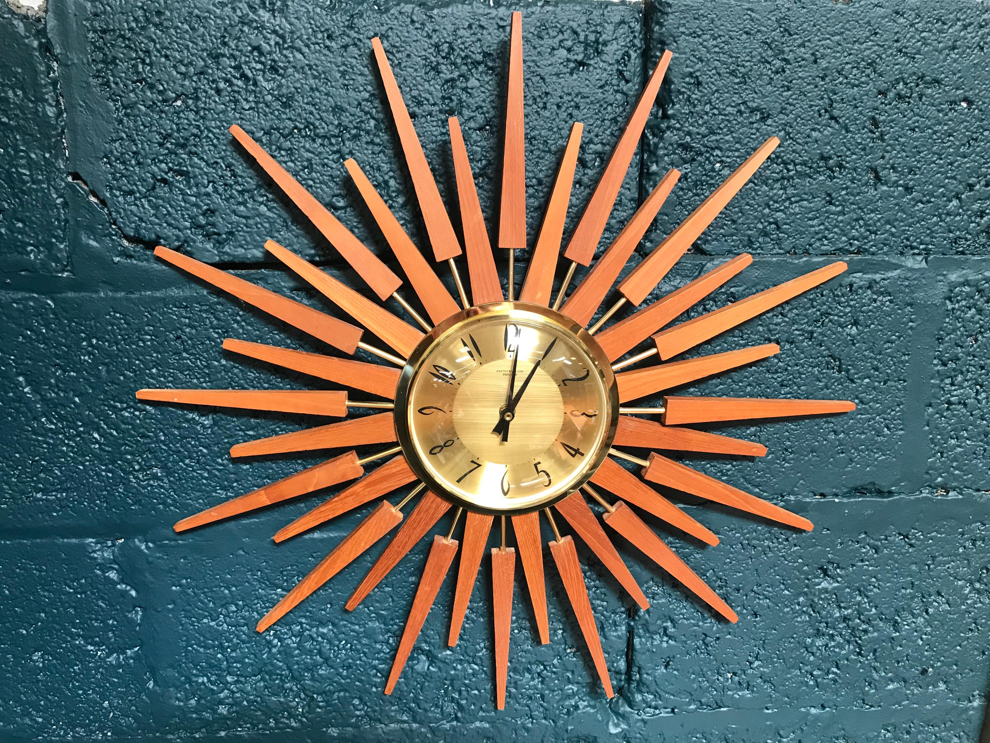 Fabulous, iconic, retro Anstey & Wilson sunburst clock. This wall clock is the most sought after sunburst/ starburst clock in the UK. A beautiful example, it has particularly nice stylized number on a brass face and a teak wooden sunburst. The