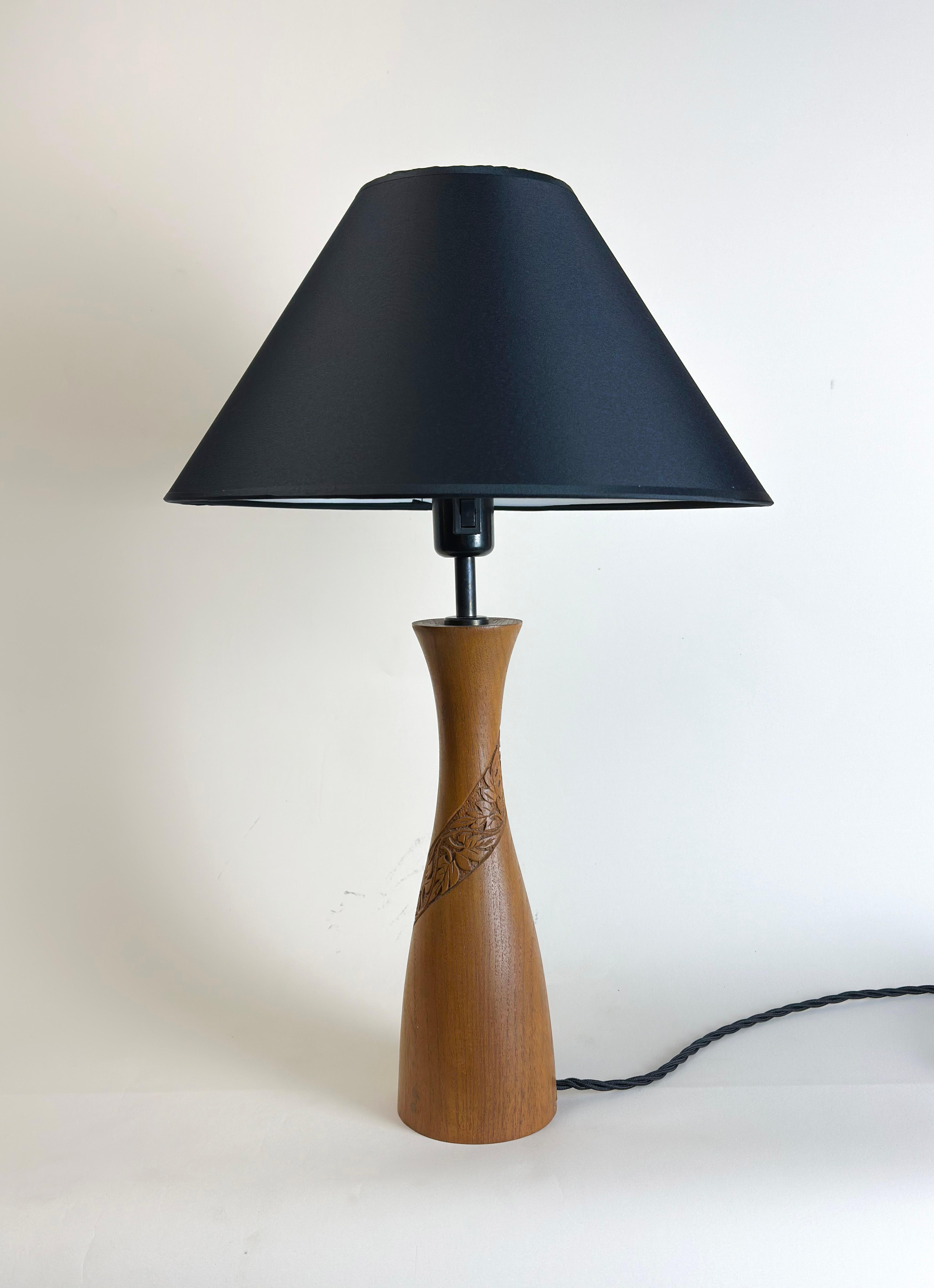 A Mid-Century Danish-style table lamp, this piece boasts a hand-turned body crafted from teak wood, adorned with exquisitely hand-carved, folk-style leaf motifs that spiral elegantly around the base.

The lamp has received modern updates, including