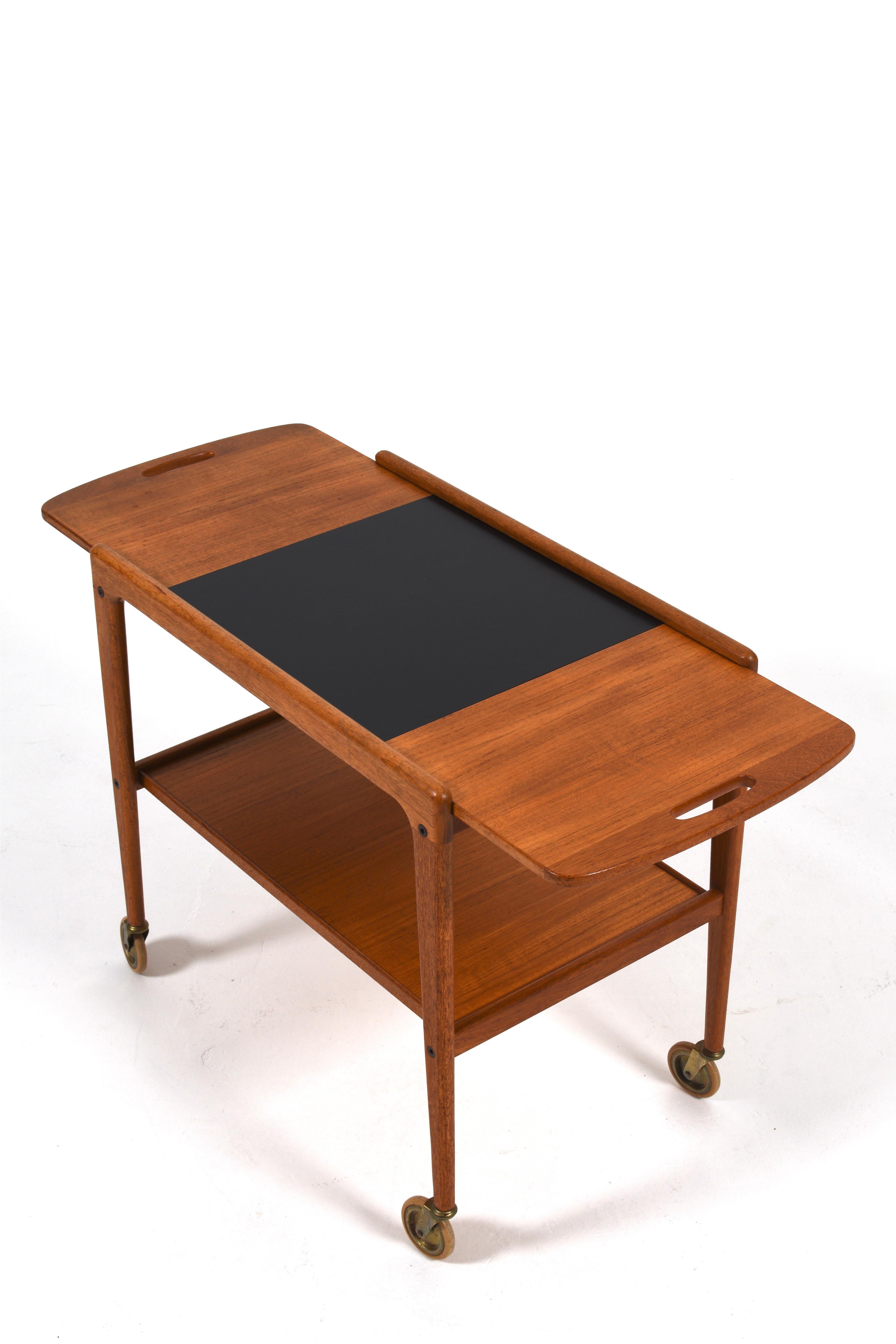 Elegant “Thea” serving trolley designed by Yngve Ekström in the 1950s, crafted in teak with a sleek black laminate top. This Swedish modern cart features softly curved edges, sculpted handles, and original brass casters for smooth mobility. With its