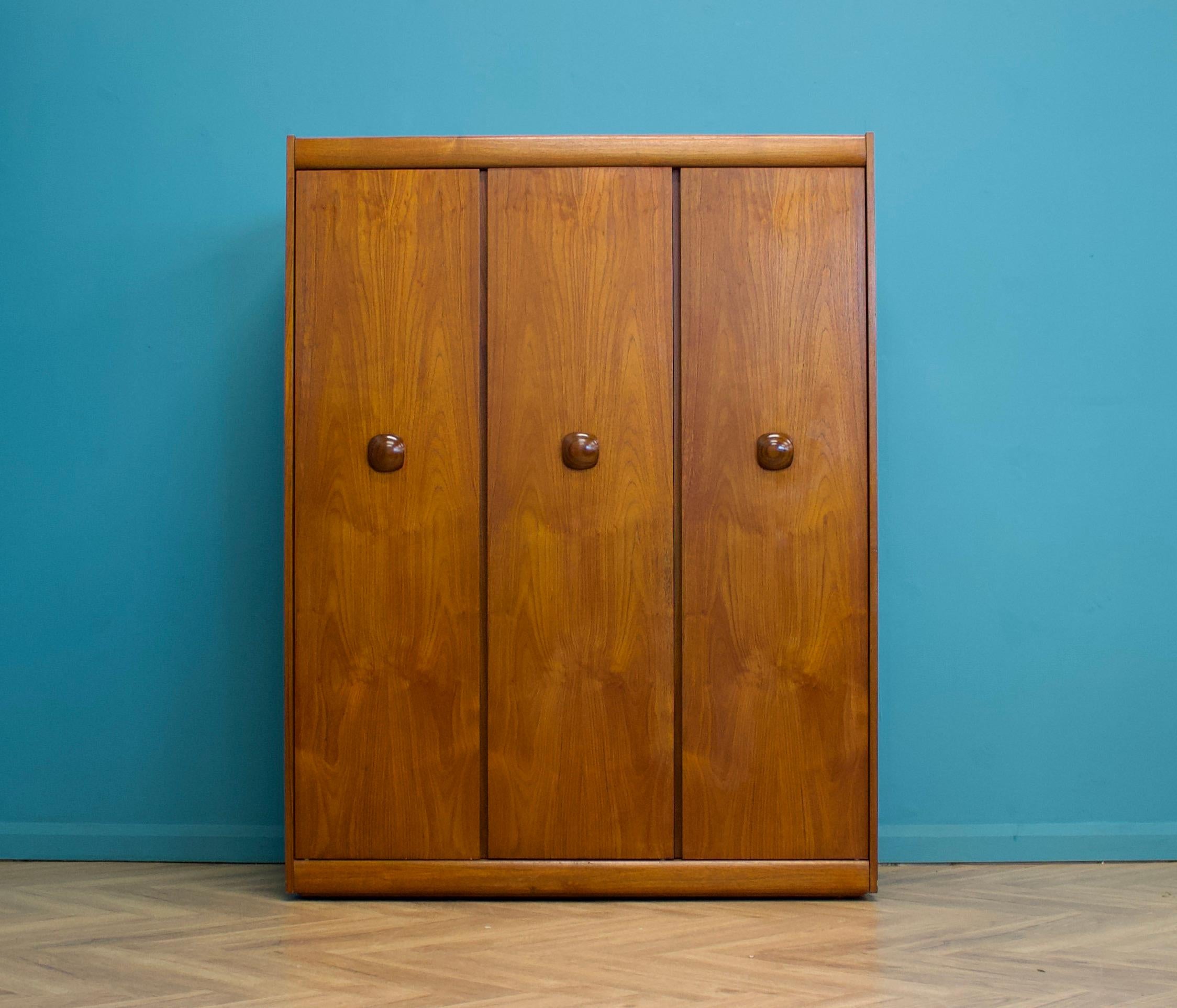 A freestanding triple door teak wardrobe from Elliots of Newbury
Made during the 1960s


Fitted out with a clothes rail
The style of this wardrobe is quite minimalist - with it's clean lines -
Featuring solid wood handles


This wardrobe can be