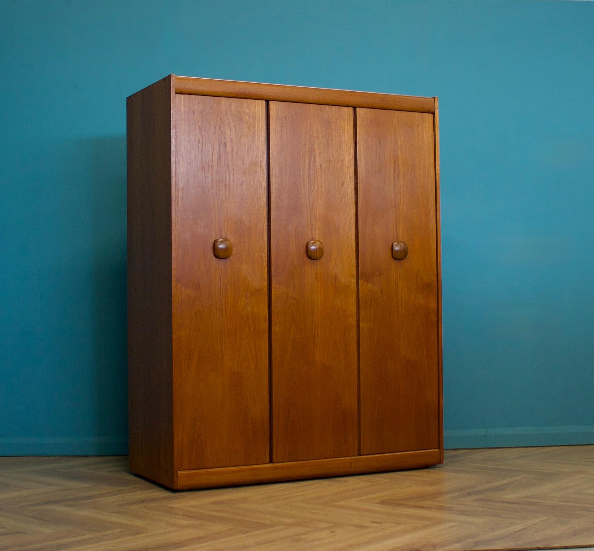 A freestanding triple door teak wardrobe from Elliots of Newbury
Made during the 1960s


Fitted out with a clothes rail
The style of this wardrobe is quite minimalist - with it's clean lines -
Featuring solid wood handles


This wardrobe can be