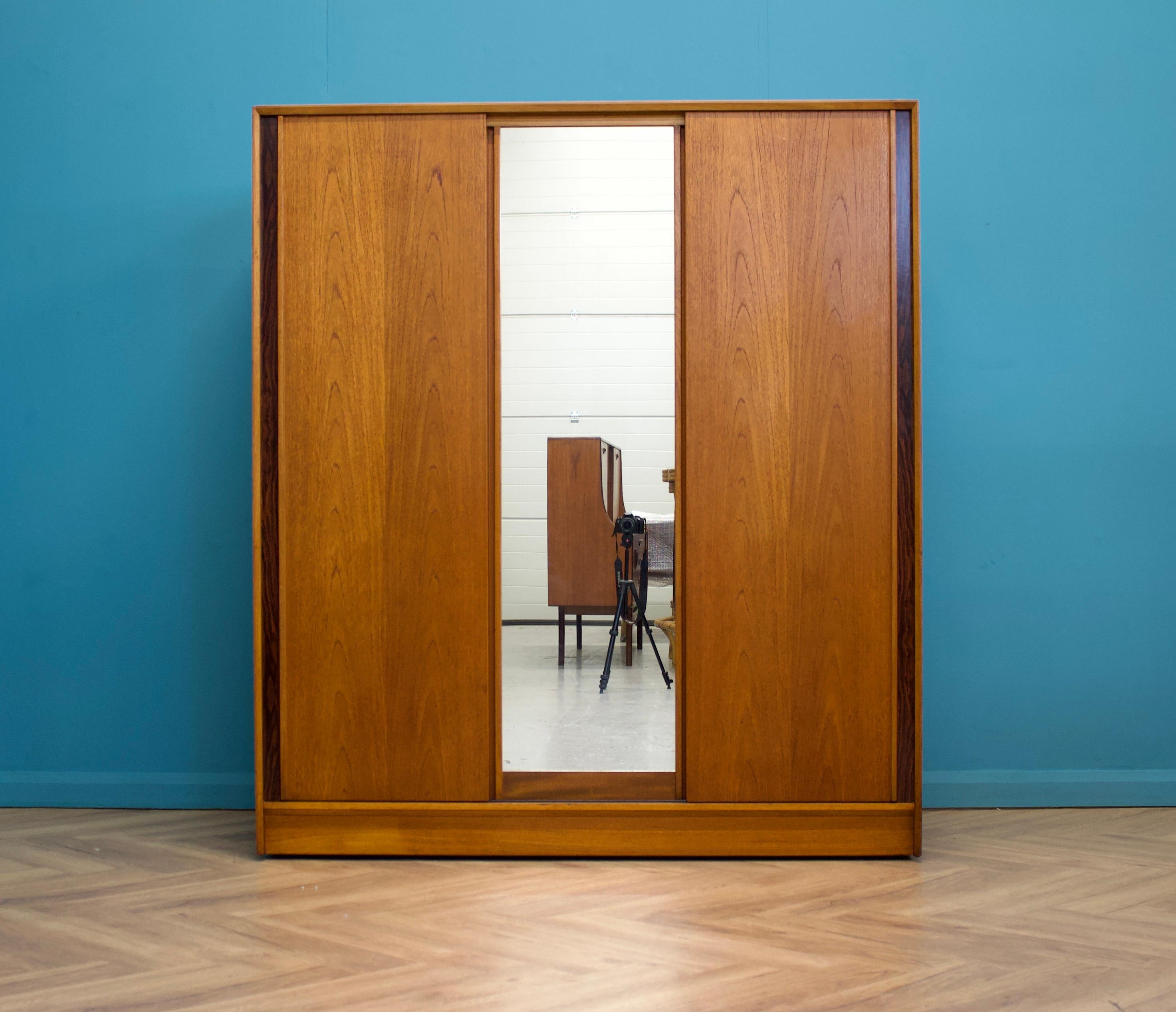 A freestanding triple sliding door teak wardrobe from Austinsuite
Made during the 1960s

Featuring walnut veneered detail to either side

Fitted out with two clothes rail to each side and shelves to the middle

The wardrobe will flat pack

There is