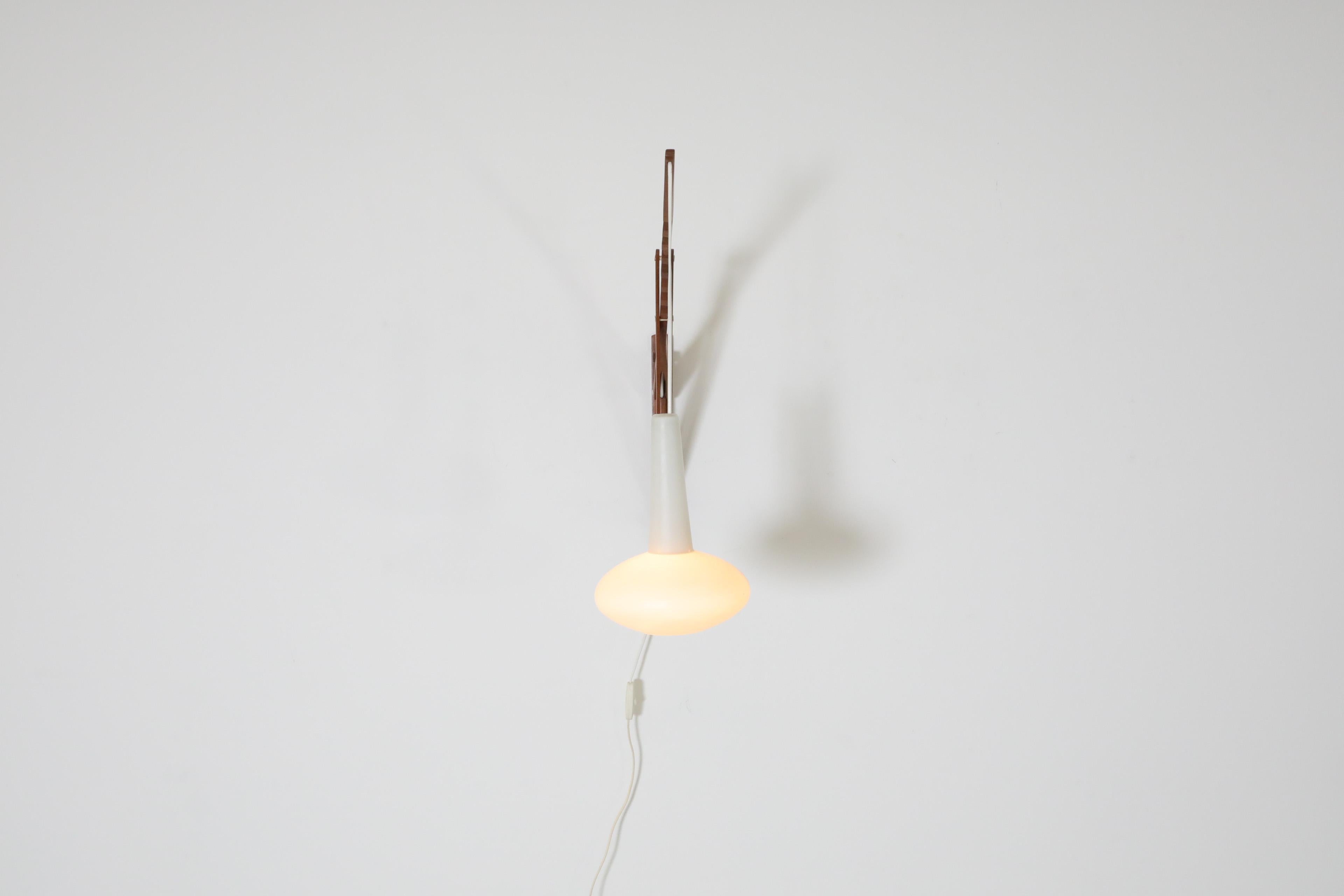 Danish Mid-century, Louis Poulsen style, teak wall mount sconce with hanging milk glass shade. This incredibly designed wall lamp is height and angle adjustable using the notches on its pole and stem. This sconce is perfect for a cozy reading space