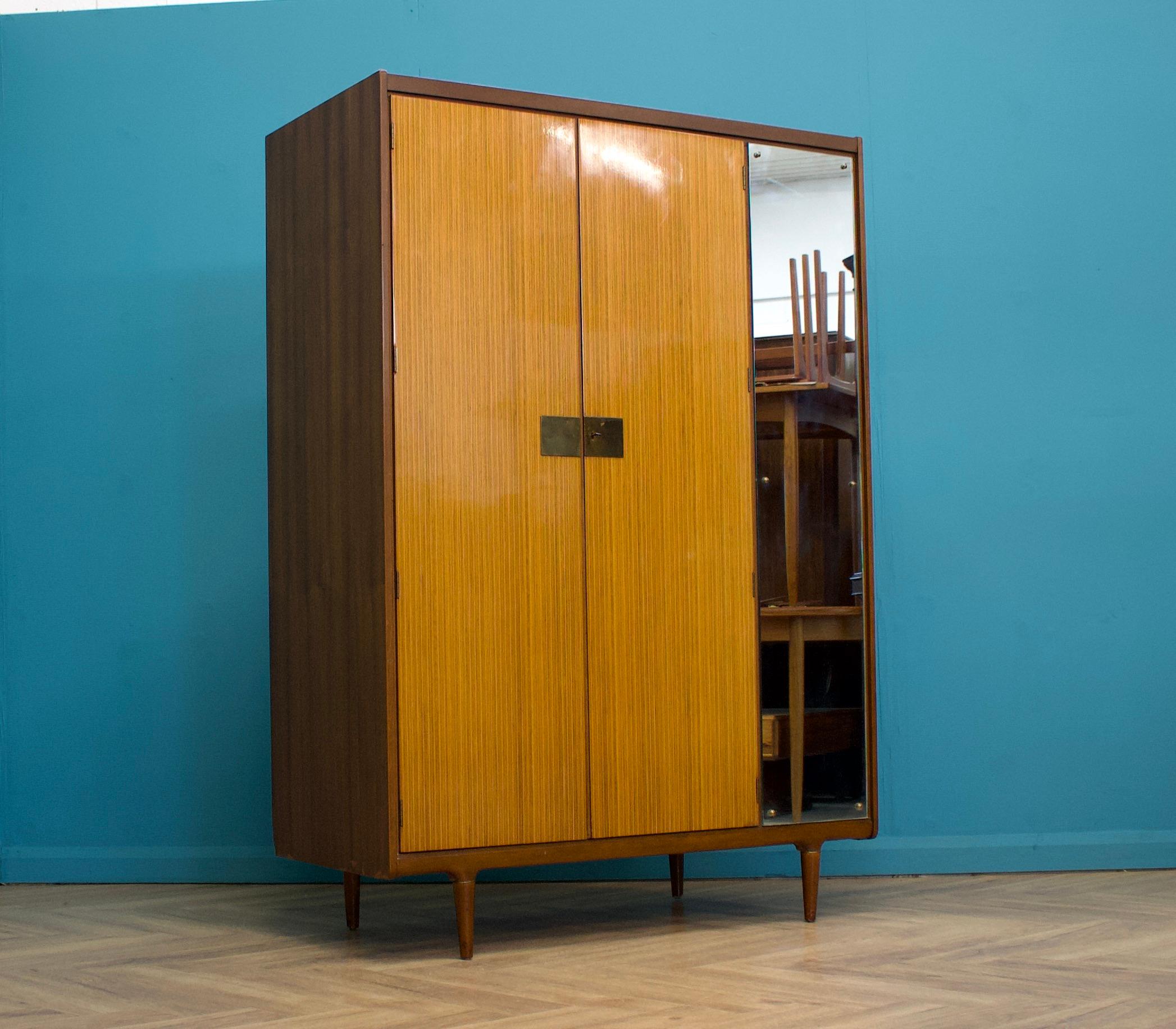 A freestanding two door teak & walnut high polish wardrobe from Wrighton -  in the Italian style
Made during the 1960s


Fitted out with a clothes rail and a full length mirror to the front


