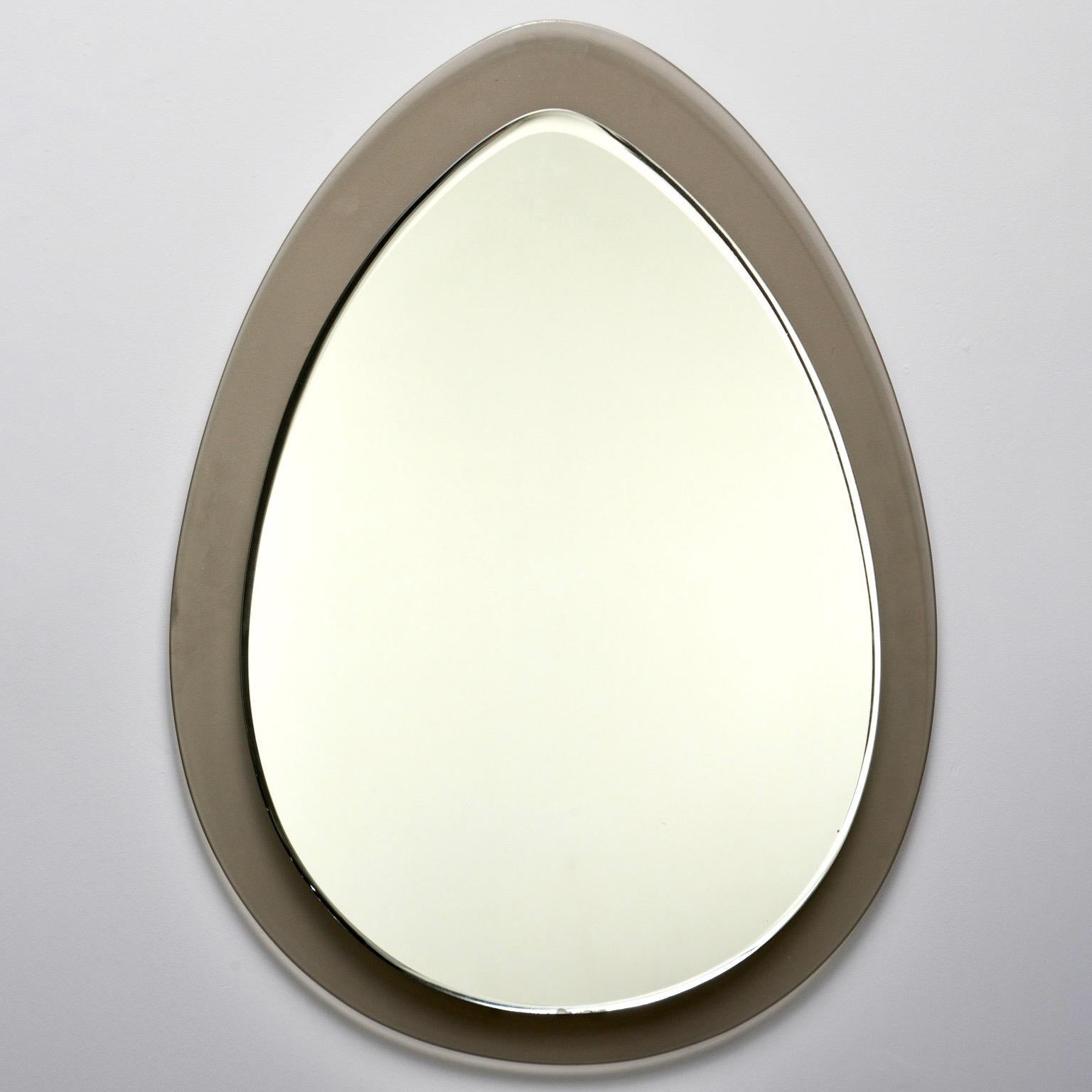 Italian wall mirror in style of Fontana Arte or crystal Arte features a tear drop shaped mirror with wide, taupe colored glass frame. Secured on back with metal hardware, circa 1970s. Unknown maker.
Actual mirror size: 27” H x 19.25” W.