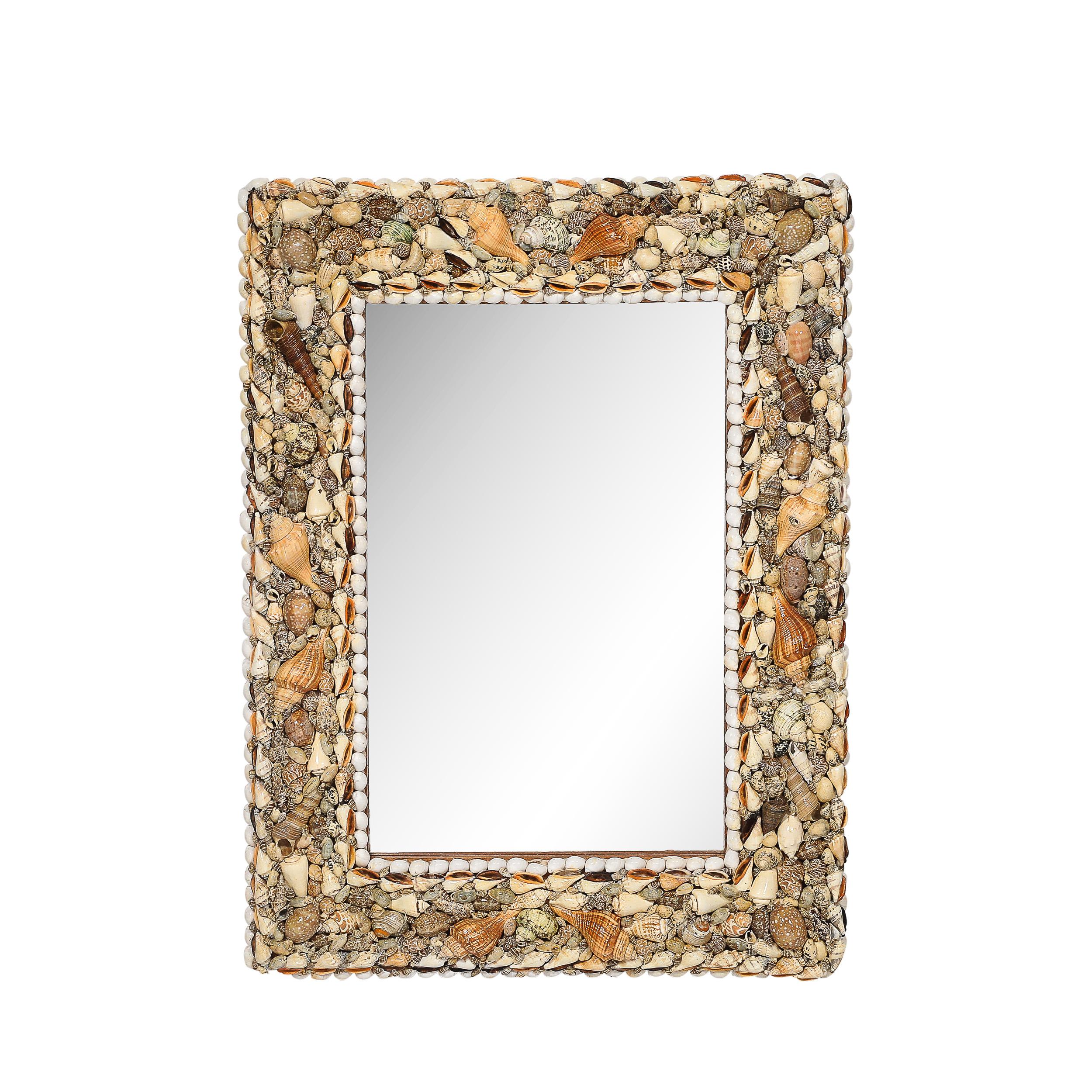This exquisite mid-century rectangular mirror from circa 1970 is crafted in the manner of Karl Springer, showcasing a masterful blend of refined materials and thoughtful execution. The frame is adorned with a tessellated sea shell pattern, featuring