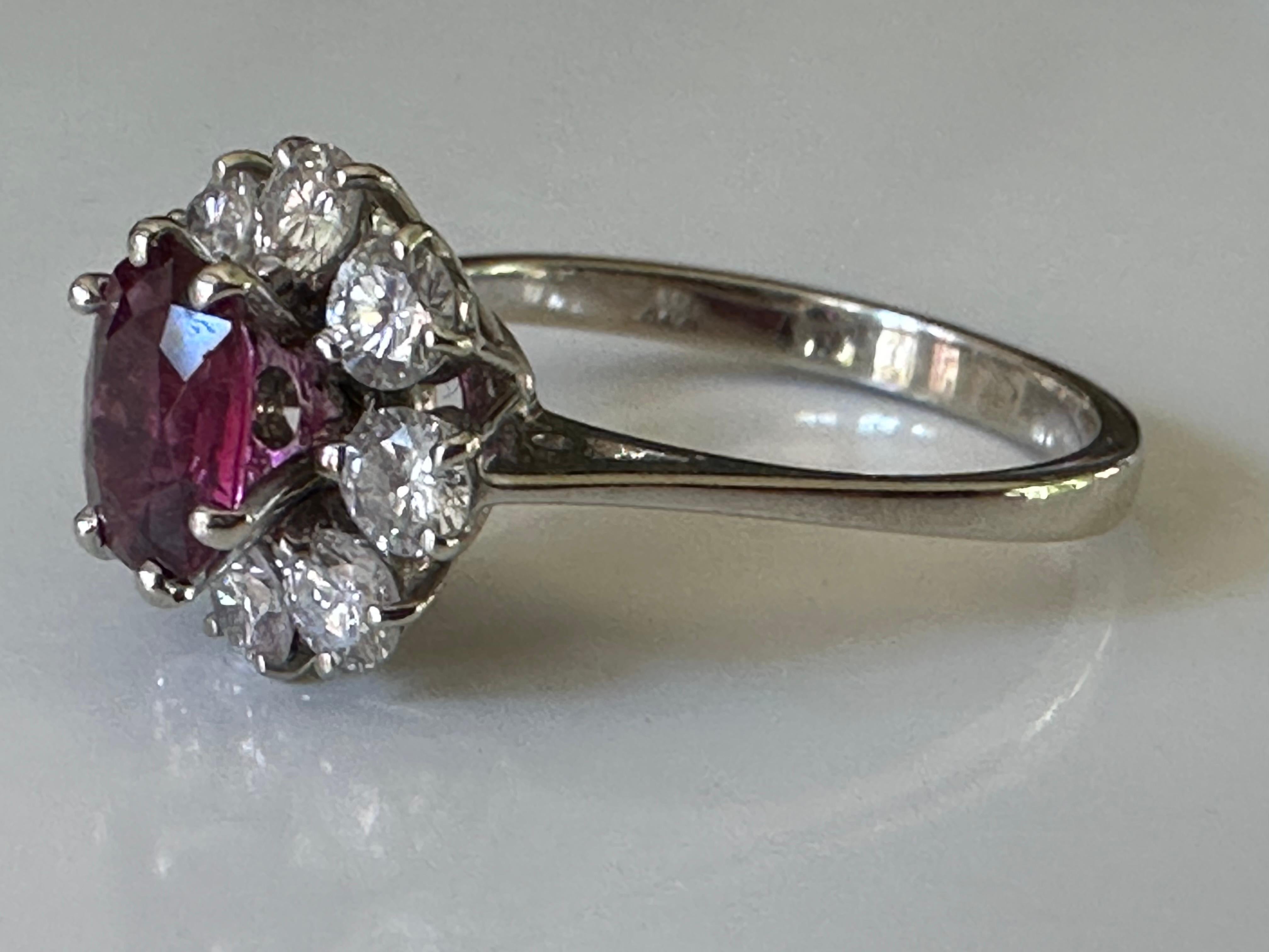 A natural oval Thai ruby measuring approximately 0.90 carats centers this exquisite mid-century ring surrounded by a floral halo of eight round brilliant-cut diamonds totaling approximately 0.56 carats. Circa 1950s. Set in 18K white gold. 

