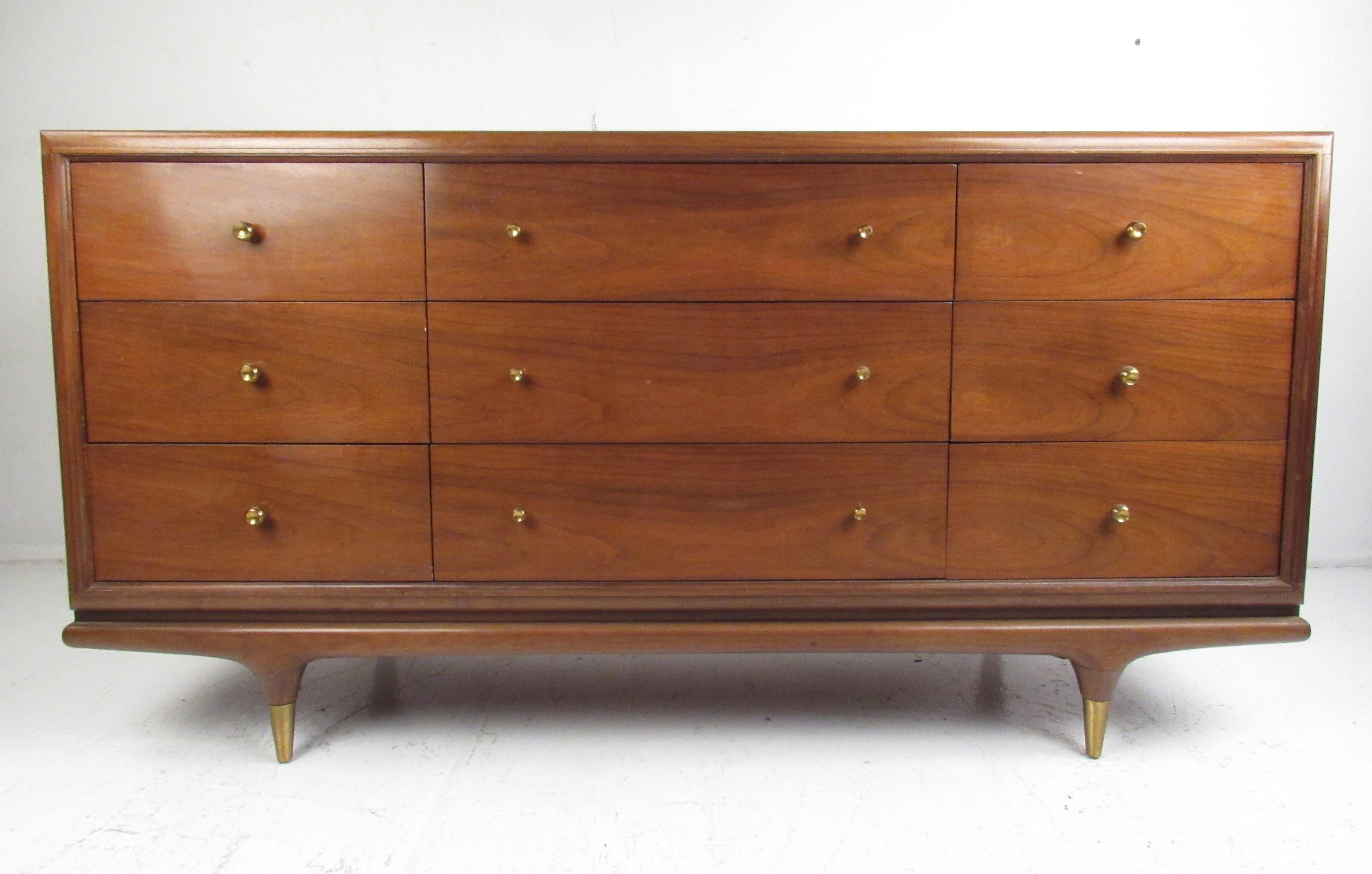 This stunning vintage modern dresser features nine hefty drawers with circular metal pulls. An extremely handsome case piece that sits on stubby tapered legs with brass capped feet. The smooth edges and elegant walnut finish make this midcentury