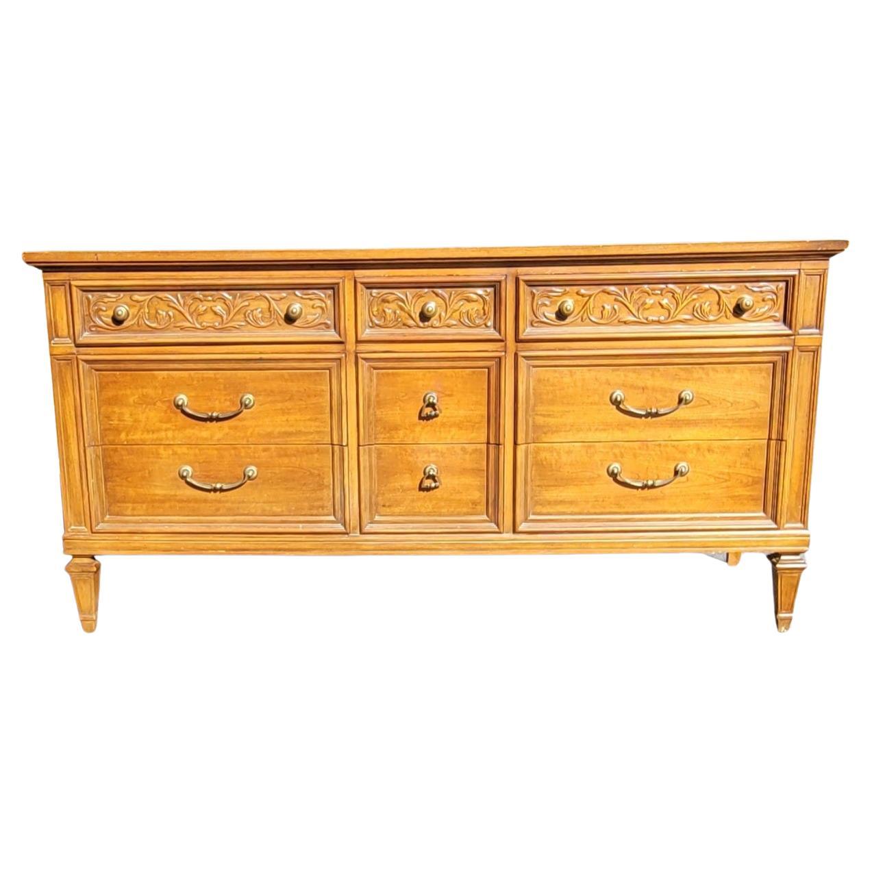 A beautiful 9-drawer Thomasville Neoclassical Style Fruitwood triple dresser in good vintage condition. Features 9  dovetailed drawers with original heavy duty drawer pulls and knobs, top drawers flanked with skillfully carved flowers throughout.