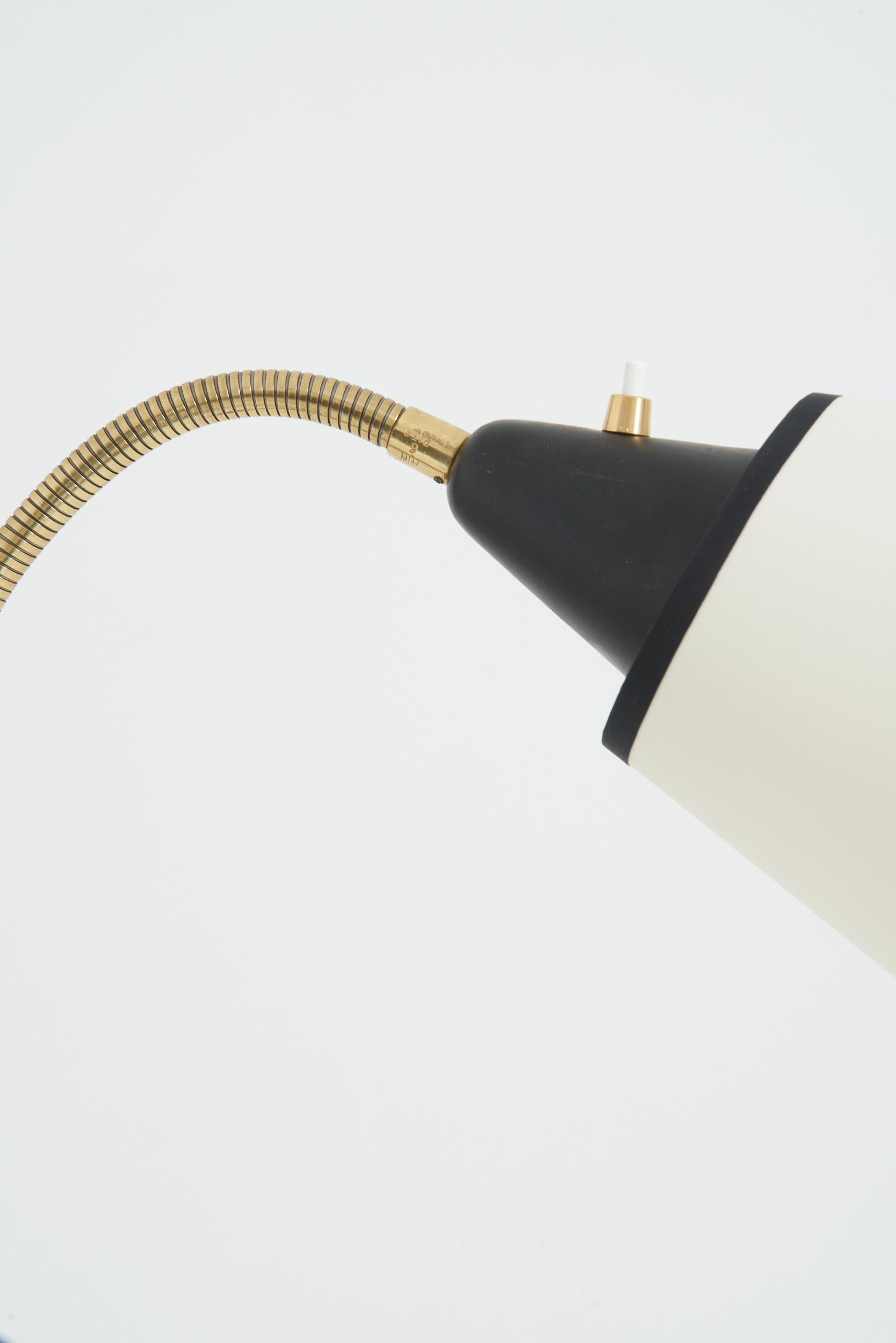 A brass and black enamelled iron three-arm floor lamp
Sweden, third quarter of the 20th Century
With the shade: 145 cm high by 104 cm wide by 65 cm depth 
Lamp base only: 145 cm high by 63 cm wide by 40 cm depth