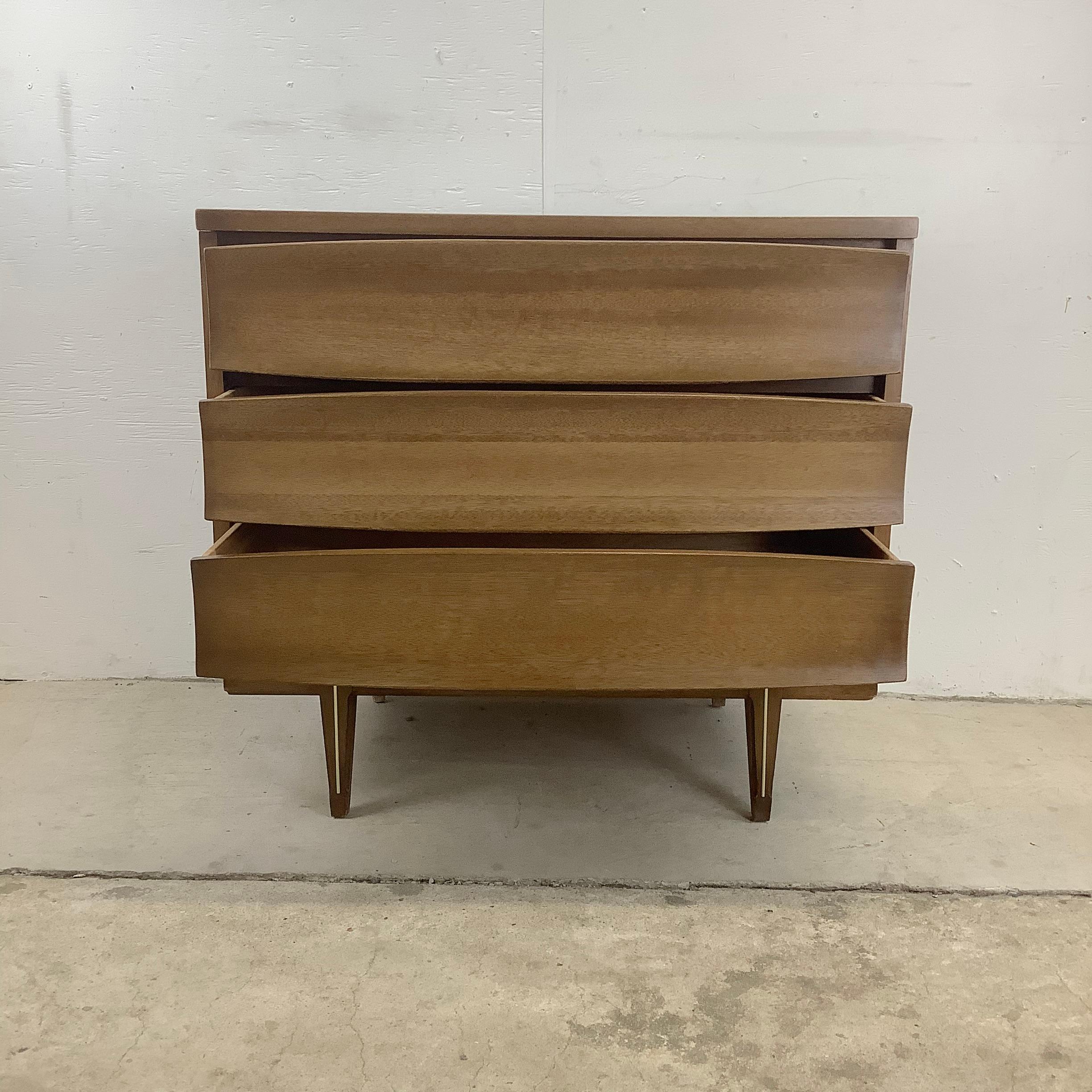 This mid-century modern three drawer chest features vintage walnut finish with concave sculptural drawer fronts and tapered legs in the manner of Johnson Carper. Perfect sized vintage dresser for adding extra storage to any setting without taking up