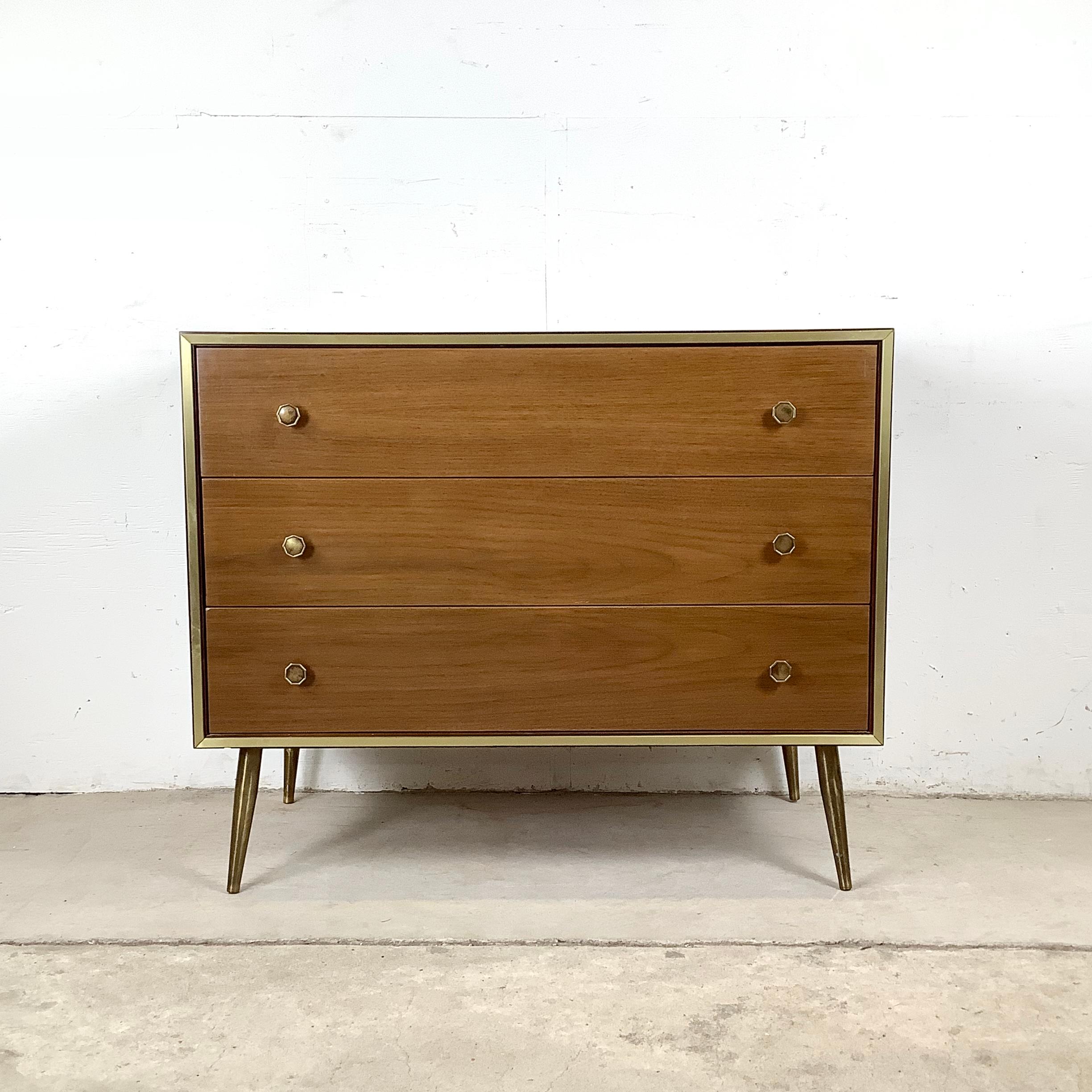 Un sofisticato studio del design di metà secolo, questo comò vintage a tre cassetti combina le calde venature del legno naturale con i dettagli in ottone. La cassa è incorniciata da sottili finiture in ottone, mentre le gambe in ottone abbinate e i