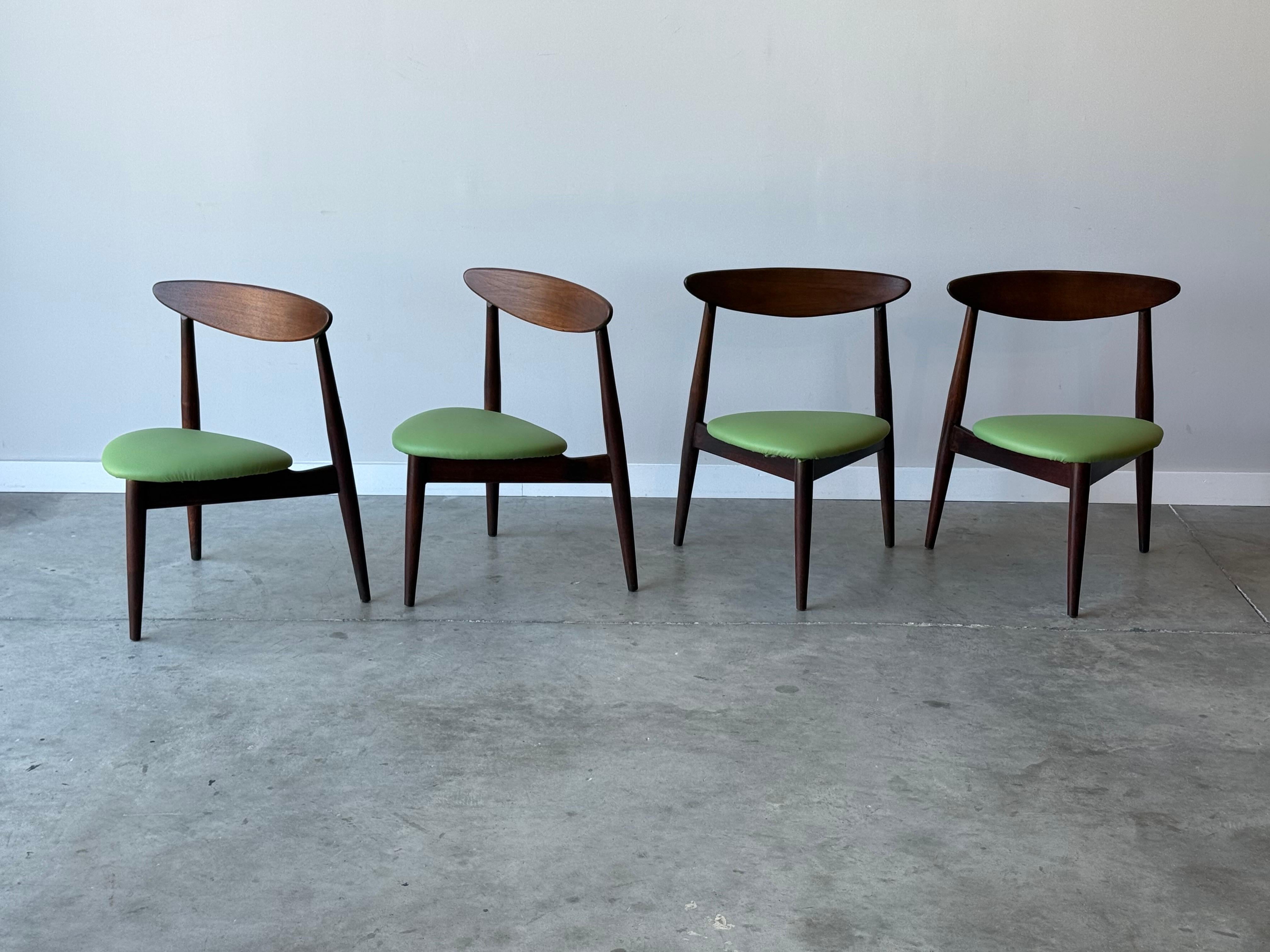 Set of four mid-century dining chairs, attributed to Hibriten with the stylings of Hans J. Wegner. A unique set with an oval shaped swoop back that creates comfortable back support. The back connects two long tapered legs that splay outwards. An