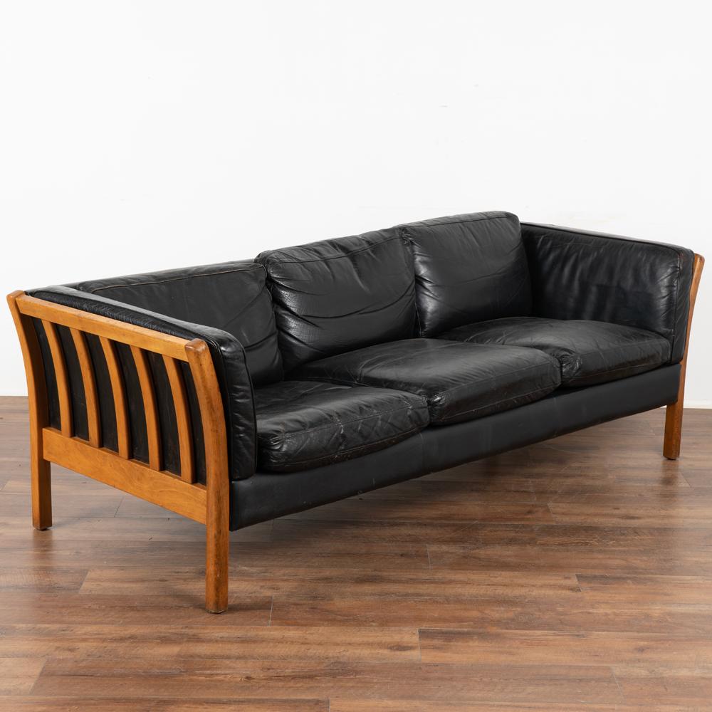 Mid-century modern Stouby three-seat black leather sofa; frame in beech with slightly curved side slats.
This comfortable sofa combines tradition with modern lines. The years of use are revealed in the aged patina of the leather, including