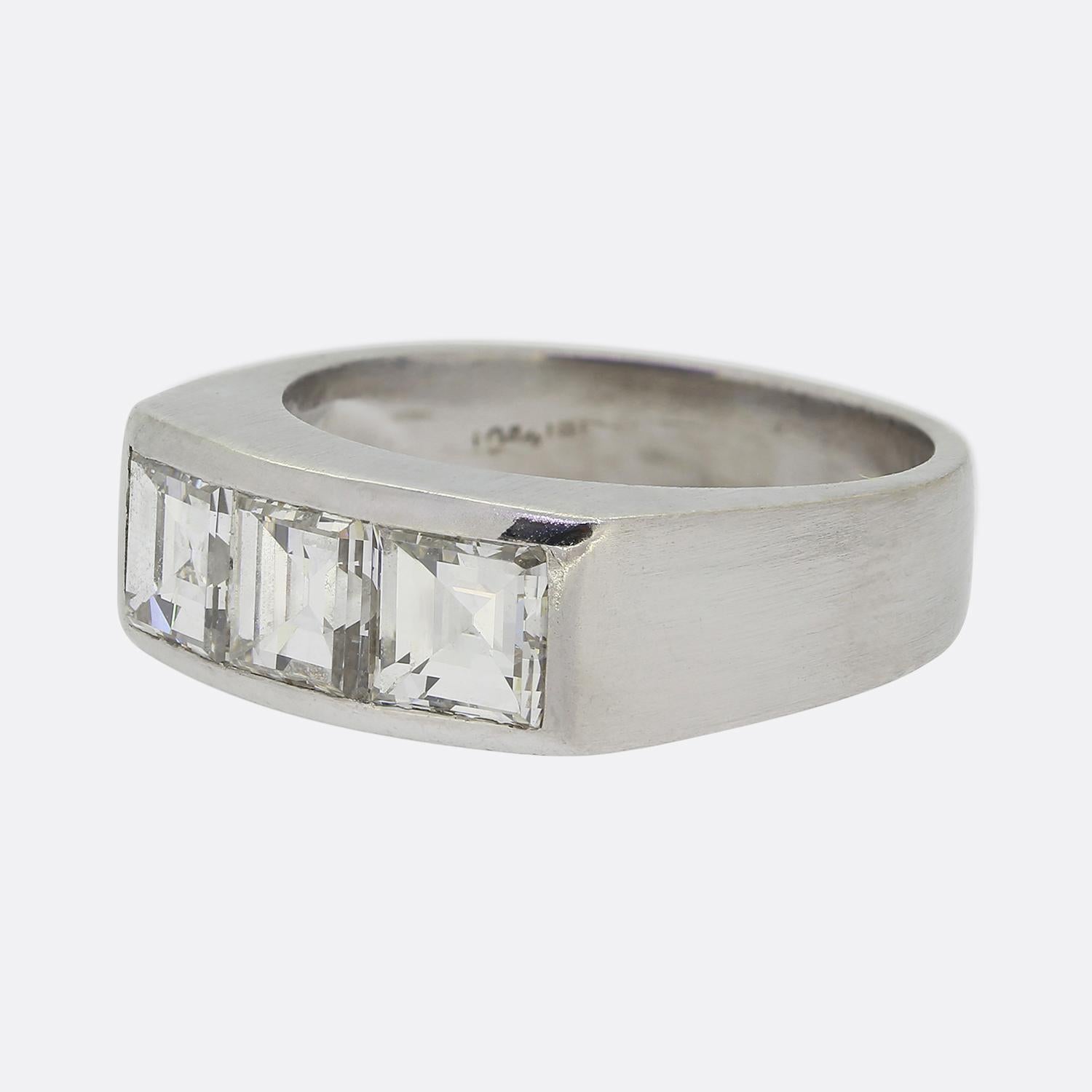 Here we have a three-stone ring featuring a trio of carré cut diamonds. This platinum piece showcases a sleek, geometric design with each bright white prominent stone being neatly channel set in a single line formation with wide square shoulders