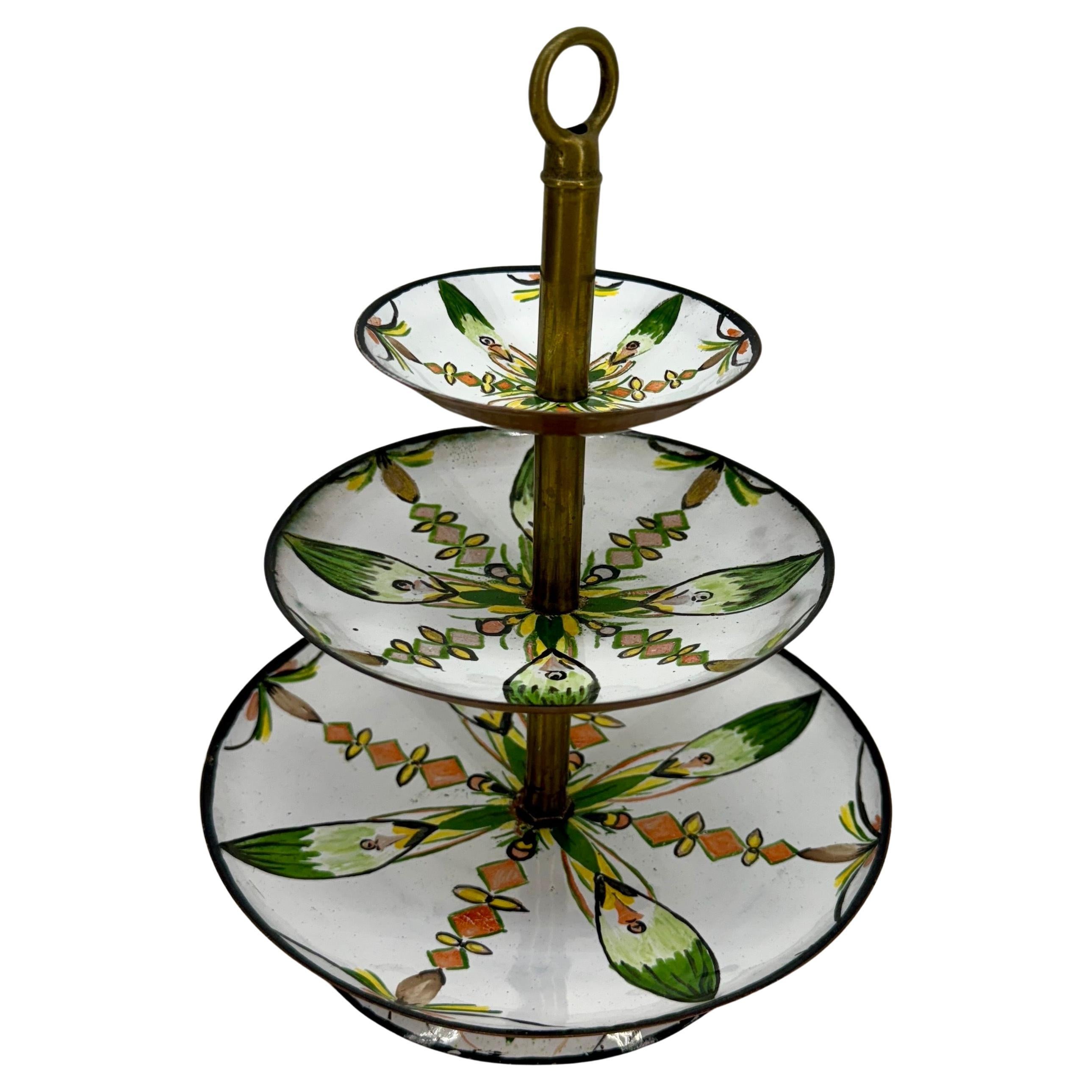 Un magnífico soporte ponderado de tres niveles. Los motivos florales verdes y naranjas están bellamente pintados a mano sobre bandejas de esmalte moldeado forradas de cobre con un asta de latón en el centro. Creemos que se fabrica en el norte de
