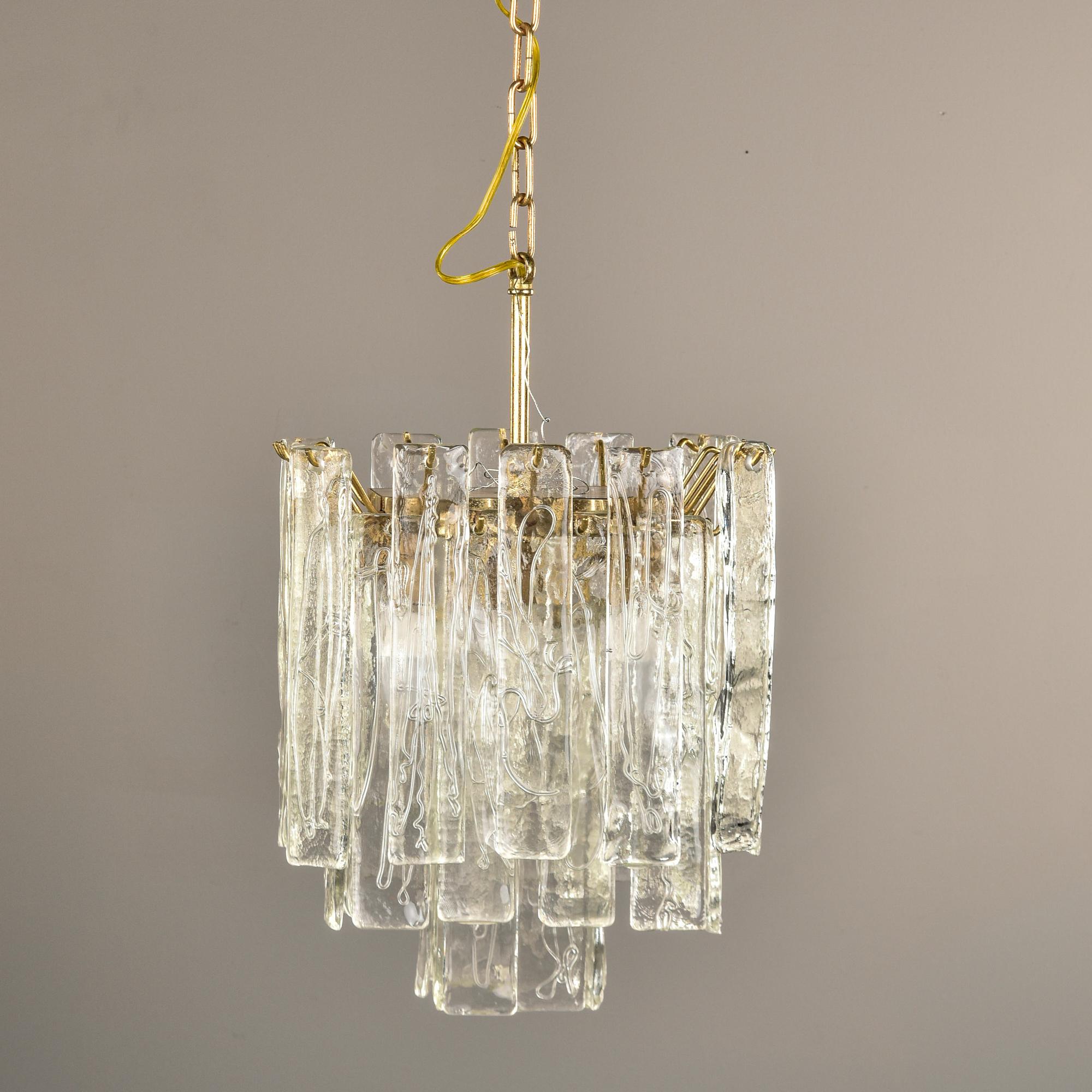 Trouvé en Italie, ce luminaire suspendu date des années 1960 et présente des pendentifs en verre de Murano suspendus à une armature en laiton poli. Les pendentifs sont rectangulaires, en verre de Murano clair avec des détails de texture de surface