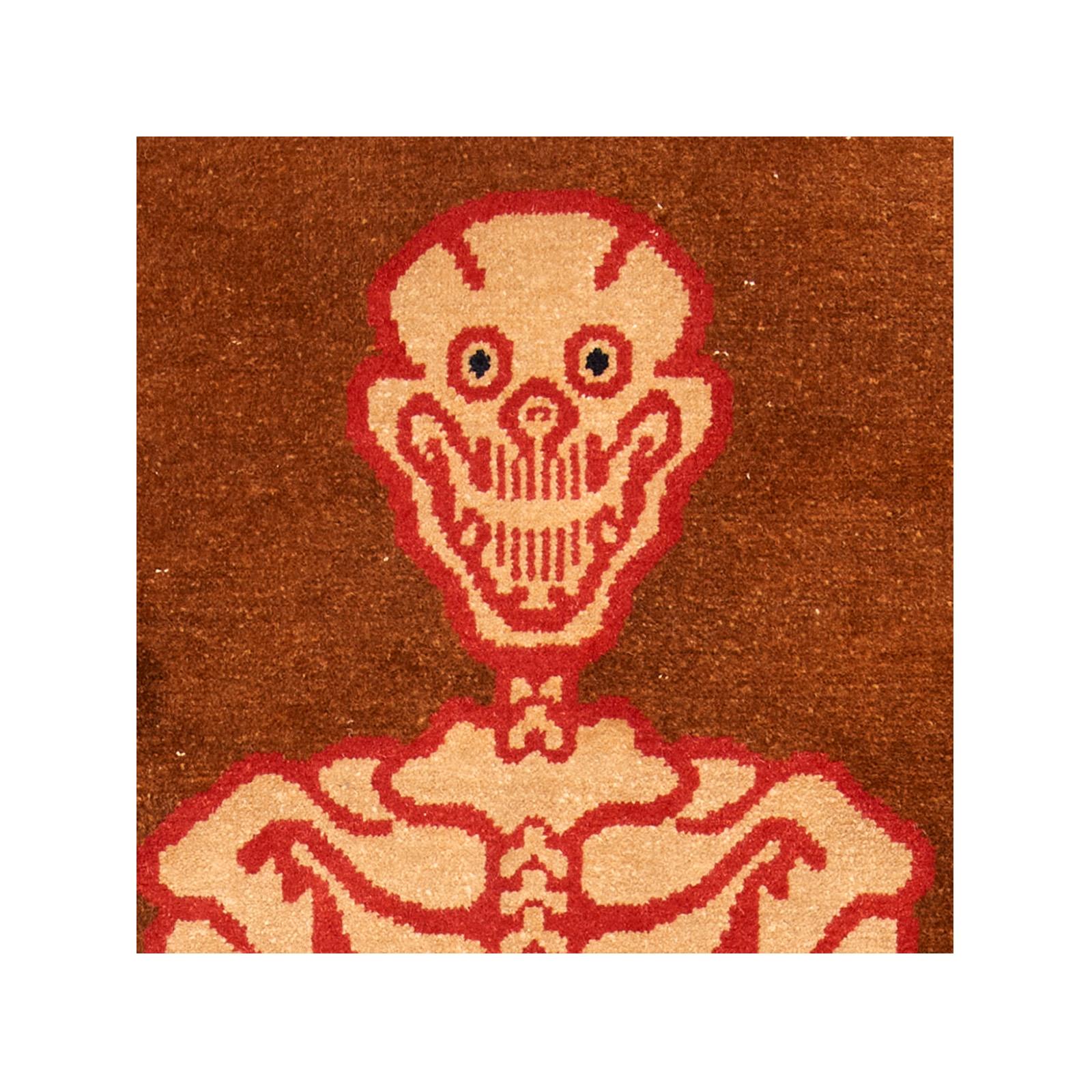 A vintage Tibetan carpet from the mid-20th century depicting a full skeleton, surrounded by a border of skulls, double dorje protective symbols, and a man's face. Ochre field with vibrant red details. This piece was likely made in Baotou, in