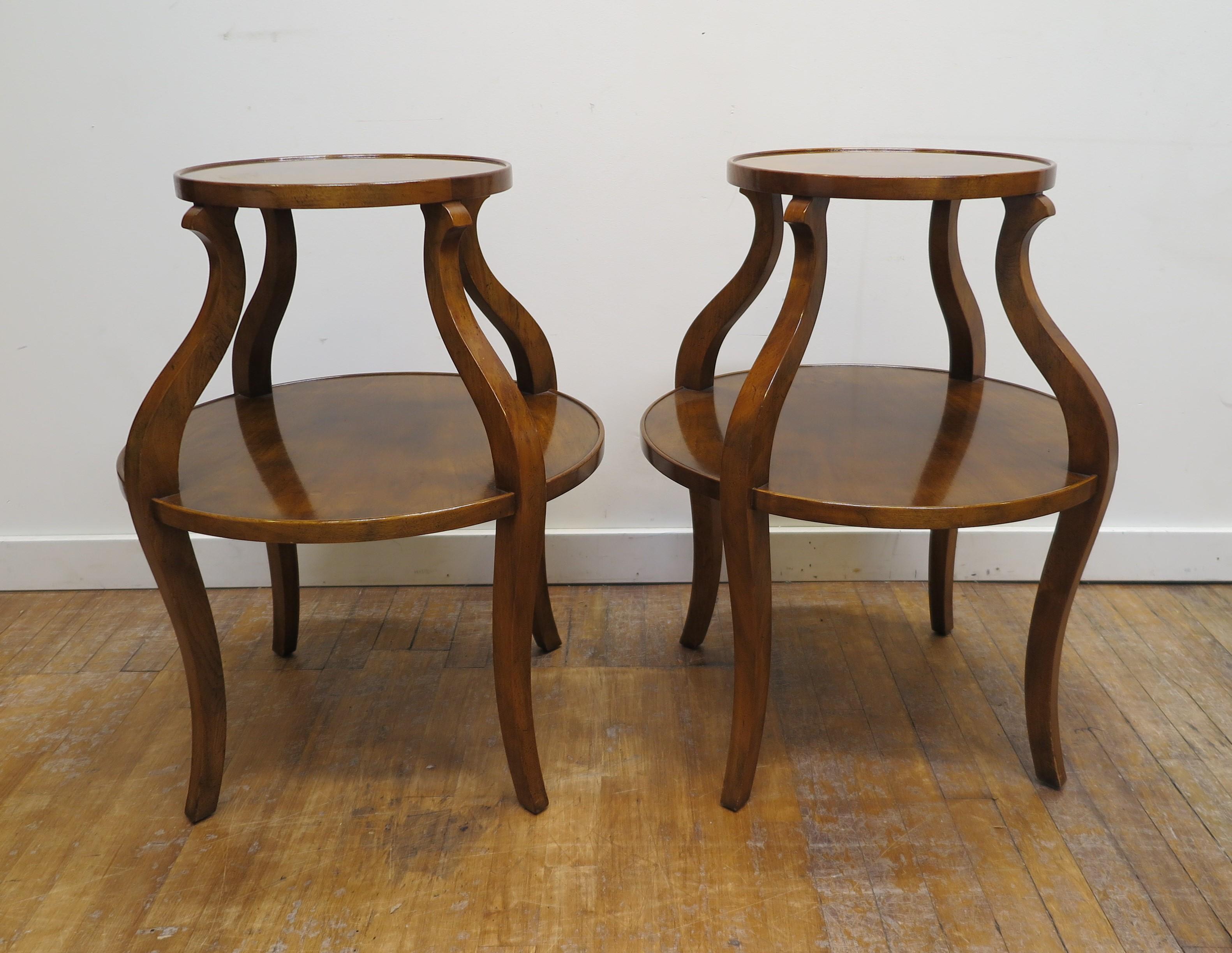 A pair of mid century Tiered round side tables. American mid century tiered round side tables in walnut. The top shelf floating set on cabriole style legs, with the lower shelf as struts. Raised lip rim to both tiers, elegantly shaped and of quality