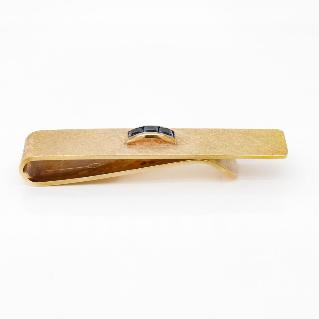 Un raffinato fermacravatte di Tiffany & Co.

In oro 14k.

Il fermacravatte ha un motivo inciso a croce con finitura Florentine ed è incastonato al centro con 3 gemme di topazio blu di Londra a taglio quadrato.

Semplicemente un grande design