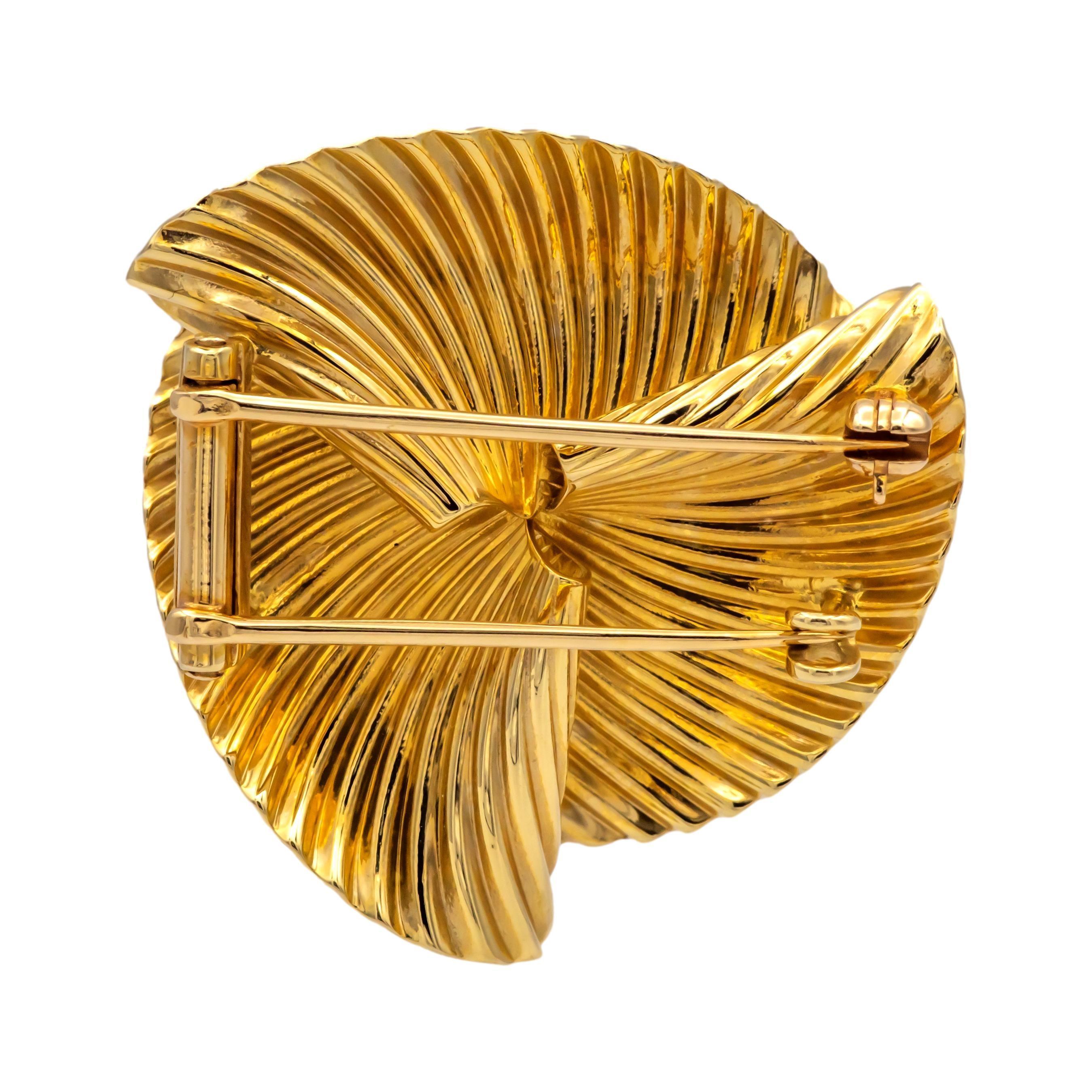 This vintage Tiffany & Co. brooch features a swirl design with ribbed radiating grooves. The ridged pattern enhances the play of light across the surface. The brooch is crafted from 14K yellow gold and is equipped with a double bar pin and hook
