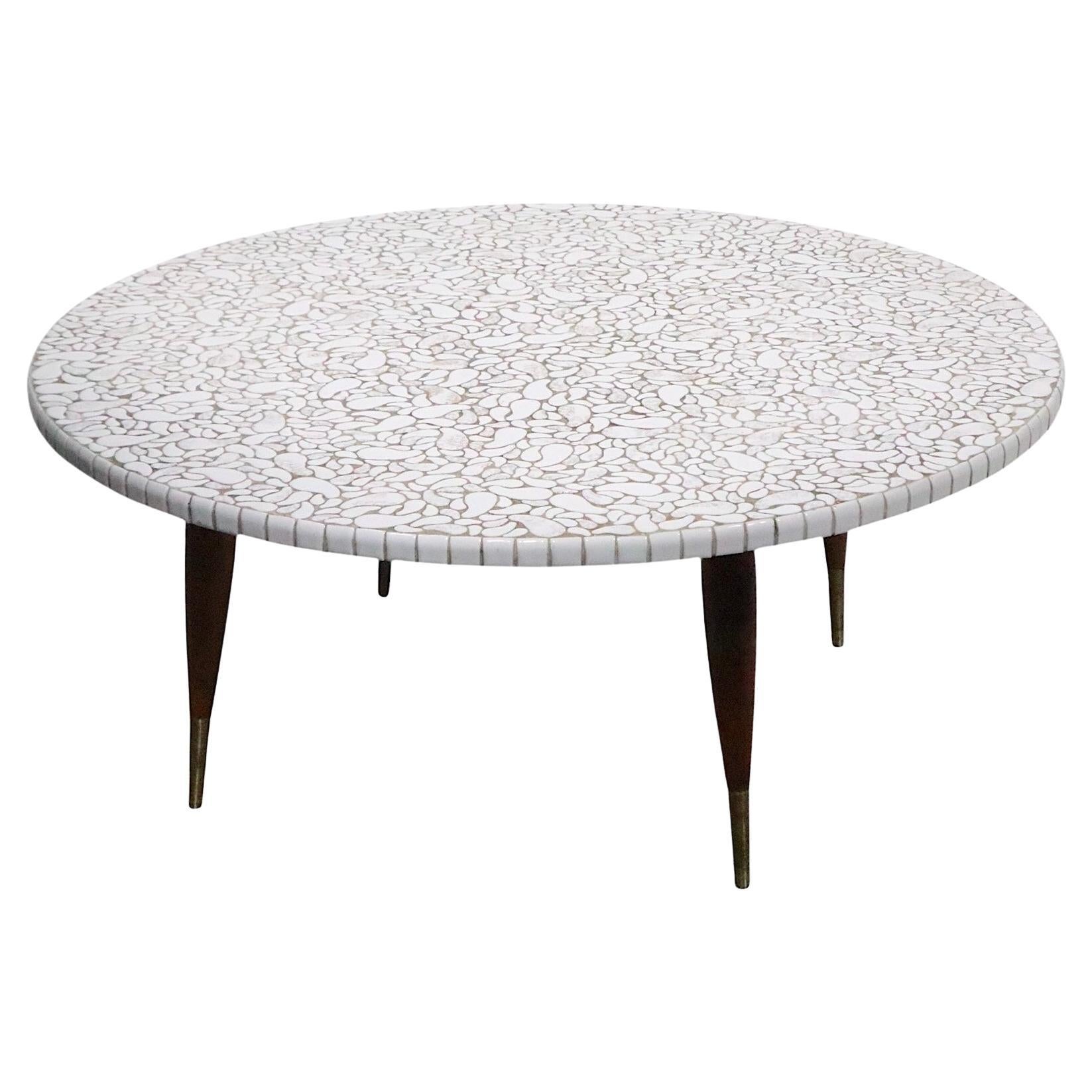 Exceptionnelle table basse du milieu du siècle en céramique, avec un plateau inhabituel en mosaïque en forme de rein, monté sur des pieds sculpturaux en bois trapézoïdal, avec des pieds gainés de laiton. Les carreaux ont une finition très glacée en 