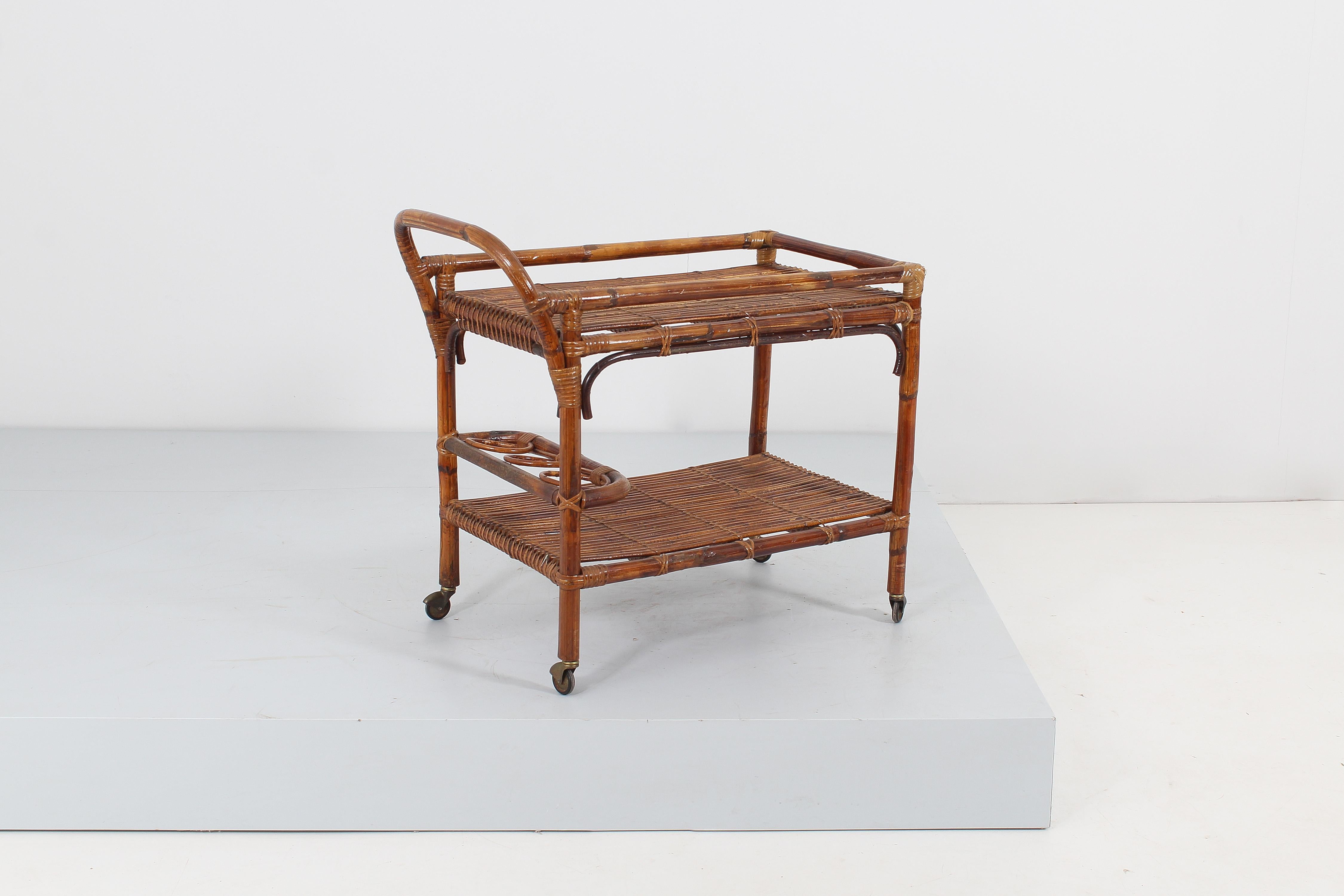 Elegant bar cart in bamboo rods and rattan, with two large shelves with bottle holder, resting on four gilt brass wheels. Attributable to Tito Agnoli for Bonacina, Italian manufacture in the 1960s
Wear consistent with age and use.