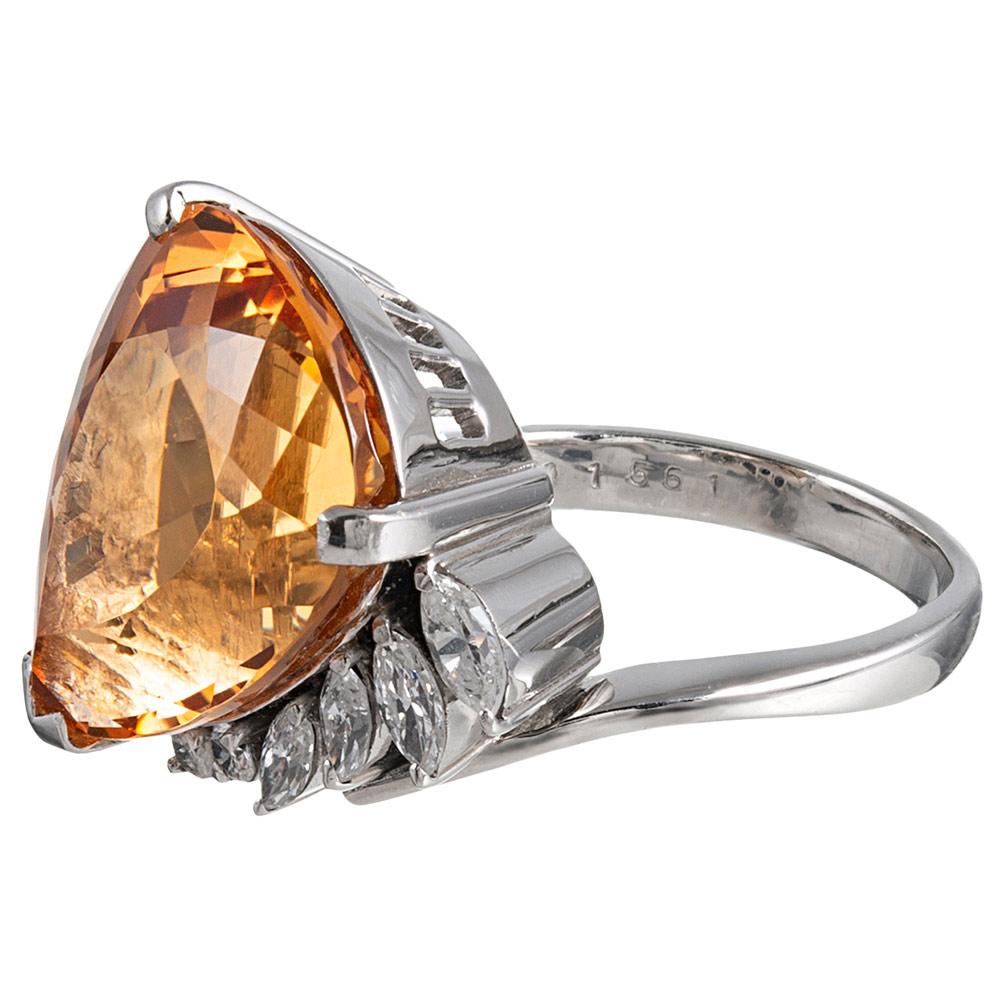 A 15.61 carat pear brilliant topaz is flattered by its platinum mounting with a tapered row of round and marquis diamonds. The asymmetric design is unusual and well-proportioned, allowing the ring to sit comfortably on the finger. The diamonds weigh