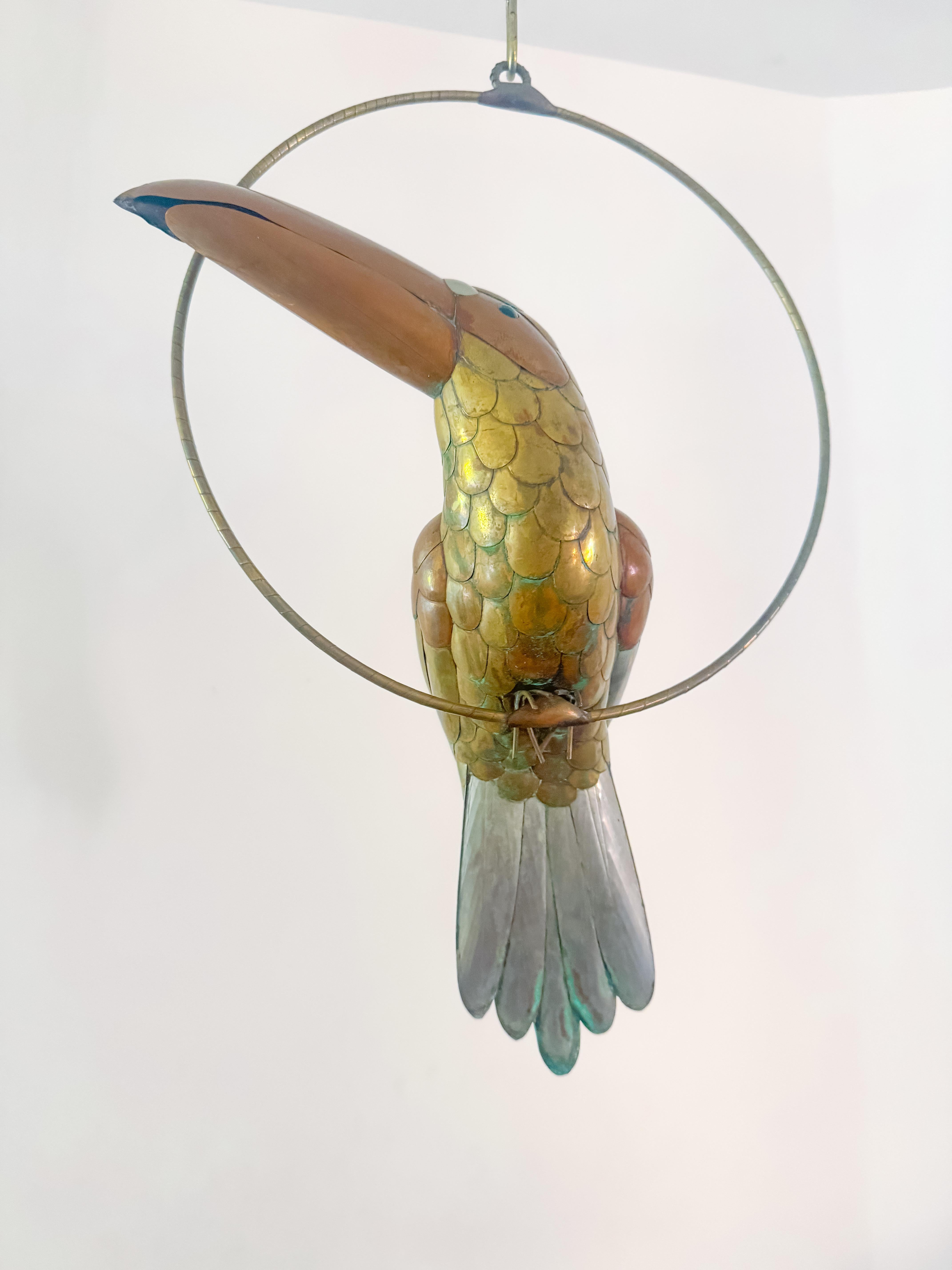 A striking vintage toucan sculpture, handcrafted in Mexico during the 1970s, in the distinctive style of Sergio Bustamante. This life-size bird is beautifully detailed in a mix of copper, brass, and silver-tone metals, with vibrant blue glass eyes