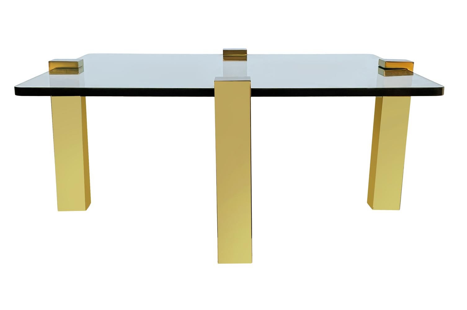 Une table de cocktail élégante et moderne datant des années 1970. Il comporte 4 pieds en laiton poli et un plateau en verre épais transparent. Le verre mesure 36 pouces de large. Les mesures ci-dessous incluent le porte-à-faux des jambes.