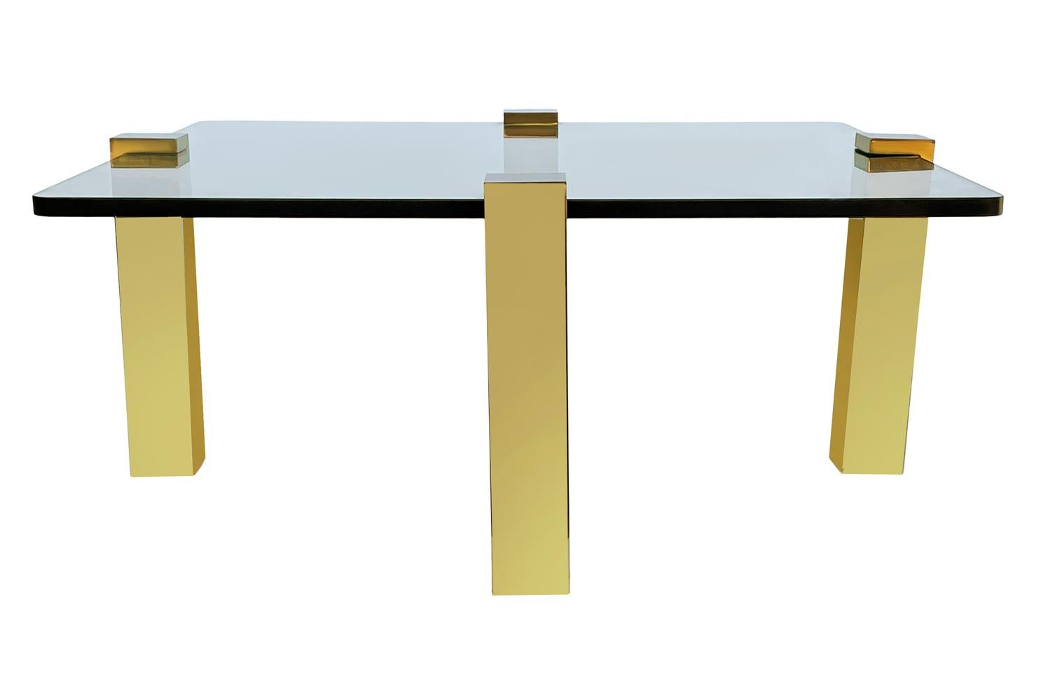 A sleek and modern cocktail table circa 1970's. It features 4 polished brass legs with thick clear glass top. Glass measures 36 inches across. Measurements below include leg overhang.