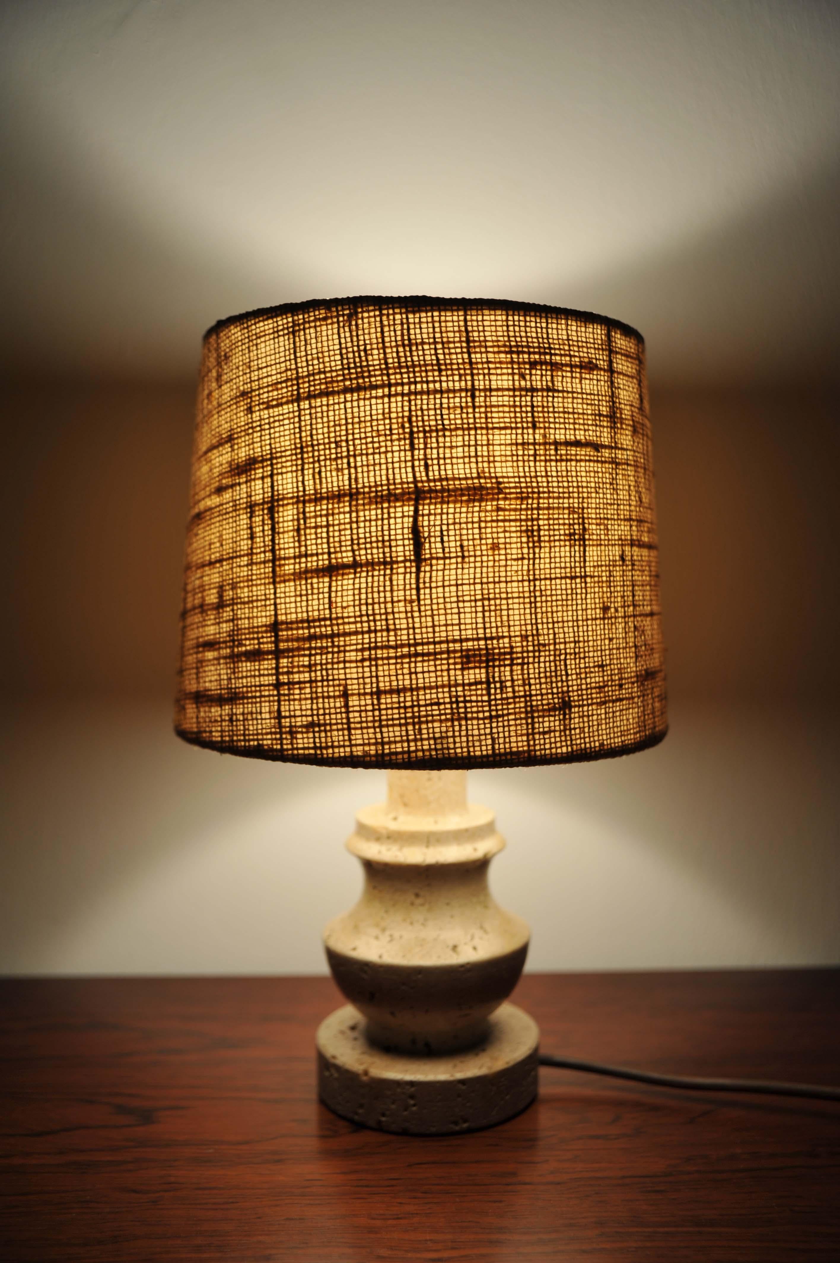 This 1960s table lamp features a sculpted travertine base with a subtle beige hue, with a cylindrical fabric shade. The lamp is in very good vintage condition, with minor signs of age-appropriate wear, and is fully functional.