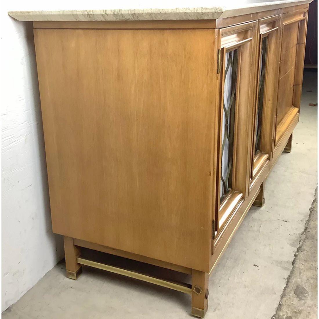 This unique Mid-Century Modern travertine top credenza features a spacious mix of three drawers and a shelved cabinet. The marble like travertine top wonderfully compliments the natural wood finish as well as the brass detail trim. Sturdy vintage