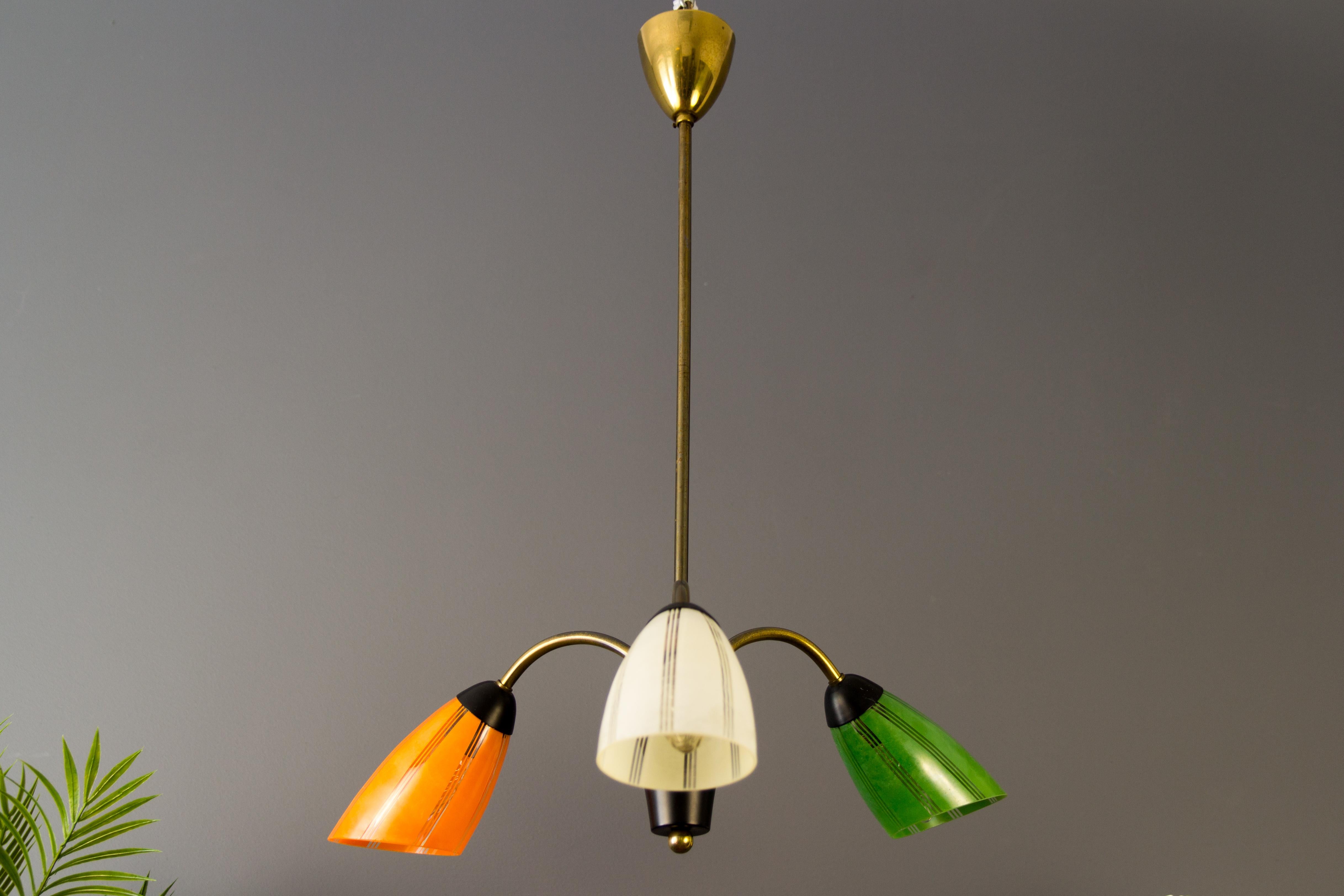 Lampe à suspension belge du milieu du siècle avec trois bras en laiton, chacun avec un abat-jour en verre de couleur différente - vert, blanc et orange - et une douille pour une ampoule E14.
Dimensions : diamètre 50 cm / 19.68 in, hauteur 85 cm /