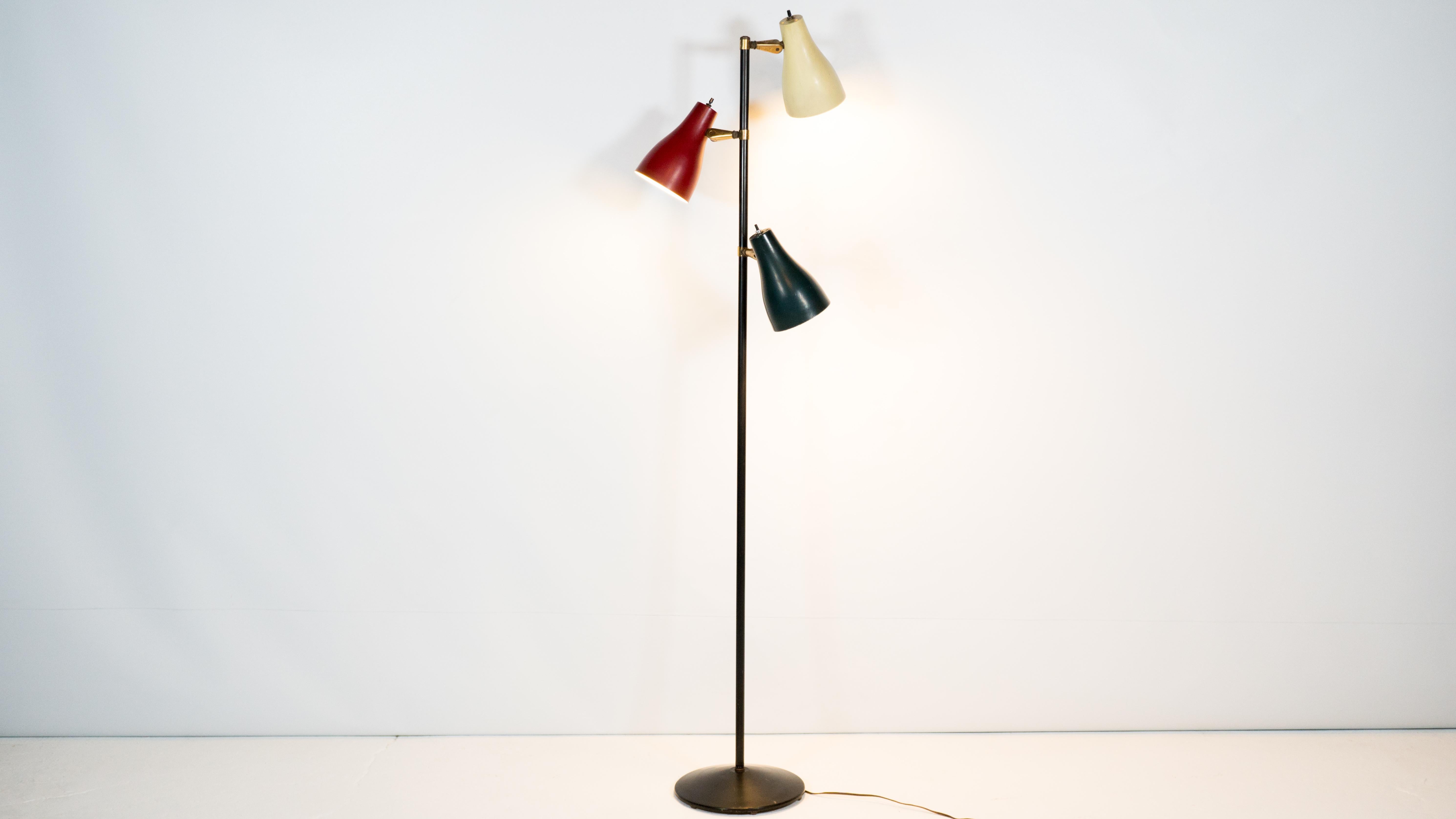 A three headed adjustable pole floor lamp with a dark green, red and creme metal shade, circa 1960s. Rare color combination. The metal pole is in a satin black with round base. Brass ring and arm details, each lamps features twist and turn type