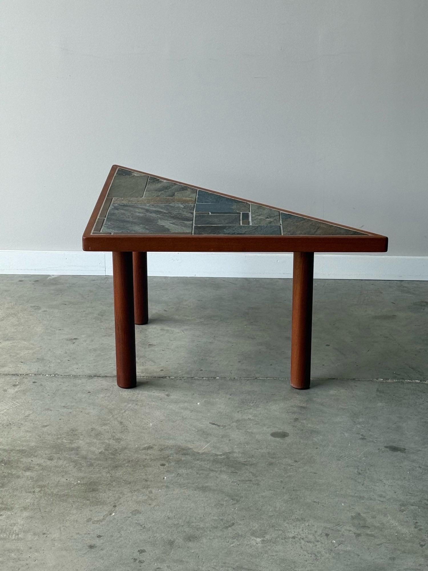 Table d'appoint du milieu du siècle, fabriquée au Danemark. Forme triangulaire unique avec plateau en pierre. Les carreaux de pierre sont principalement gris-vert. Un beau mélange de matériaux avec de longs pieds massifs en teck et une bordure en