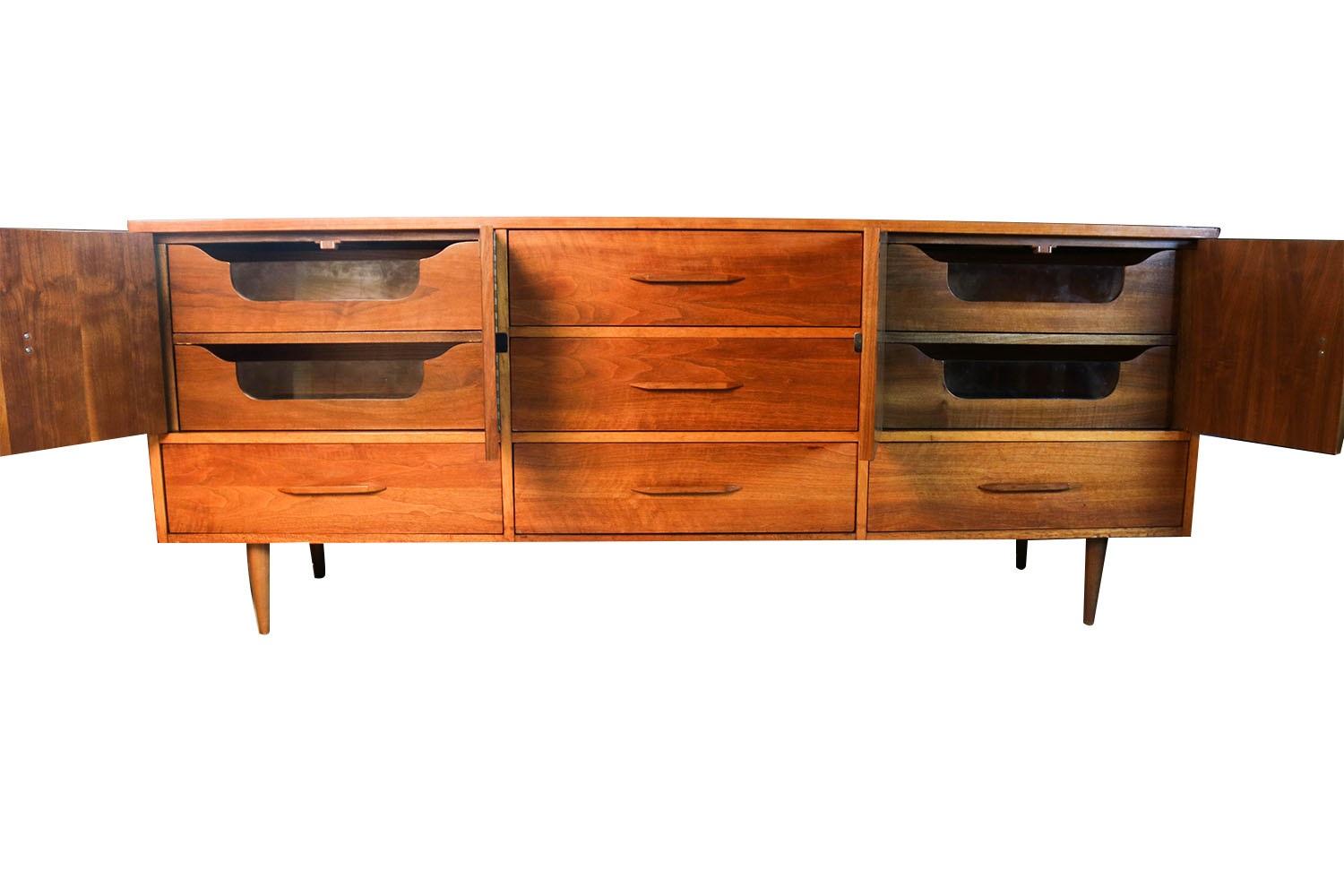 A Mid-Century Modern mixed wood triple dresser. This distinctive 9-drawer dresser with a Minimalist design allows for ample storage in a modest footprint. A simple and elegant dresser featuring 3 center drawers that are flaked by a set of double