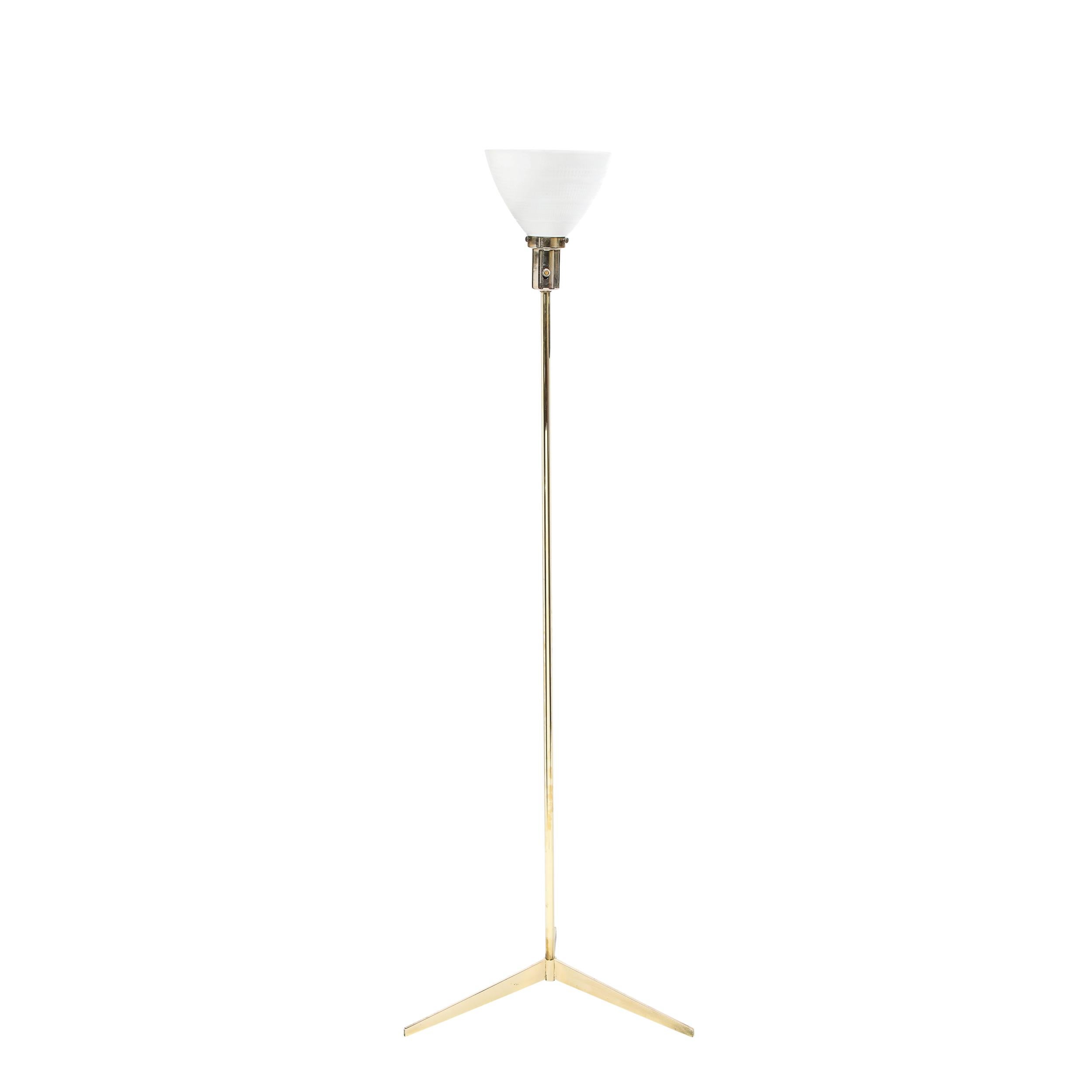 This elegant Mid-Century Modern floor lamp was designed by Paul McCobb in the United States circa 1950. It features an atomic tripod base with a cylindrical body all in polished brass. The lamp culminates in a domed textured white glass shade. This