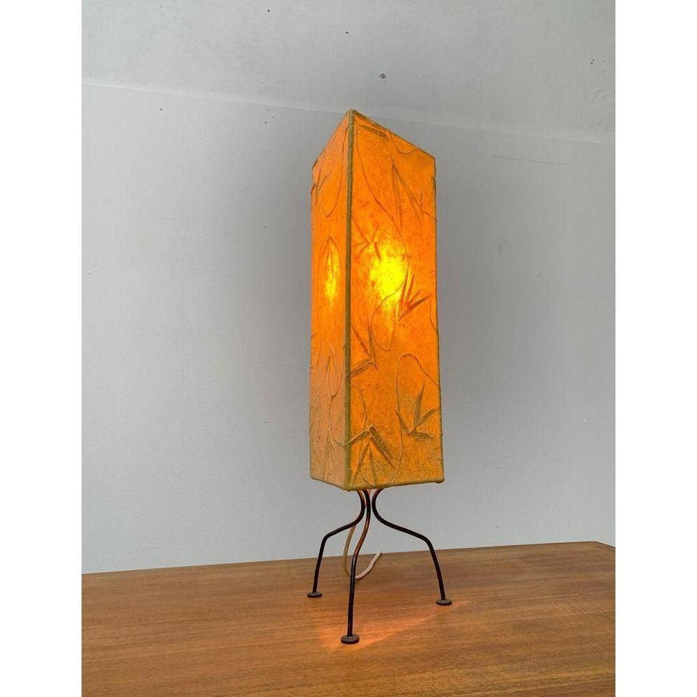 Filigree mid-century tripod table lamp.

The design shows an almost living appearance. The prism-shaped diffuser shade is made of a kind of paper, in which floral objects are incorporated. The legs of the finely crafted Tripod frame protrude from