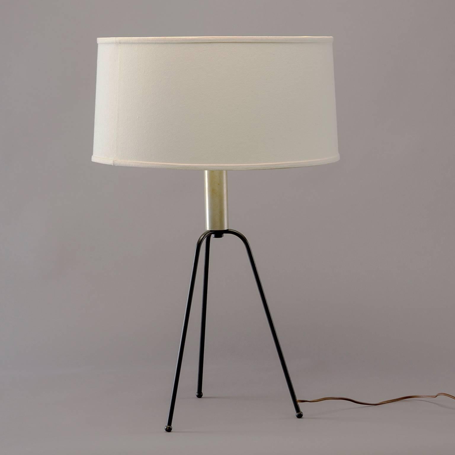 Table lamp has Minimalist black iron tripod base, brass socket piece and off-white drum shade with notched spokes designed to fit securely on glass globe beneath, circa 1950s. Measurements shown include shade. Wiring as found - test and works.