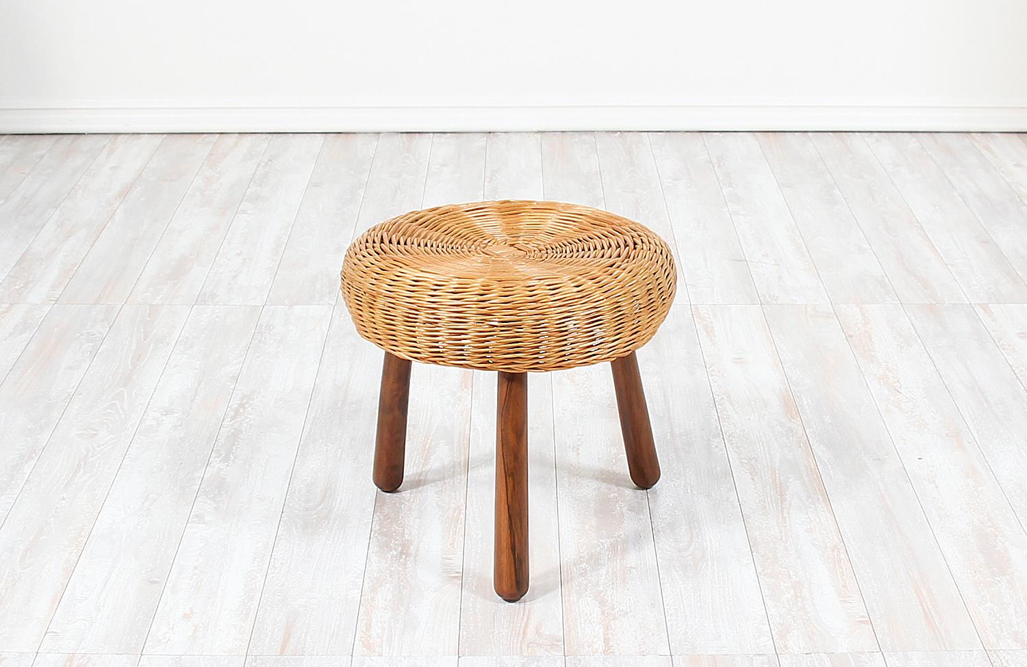 Mid-Century Modern tripod stool designed and manufactured in the United States, circa 1960s. This versatile wicker stool features its original round wicker top supported by walnut wood tripod legs with vibrant grain patterns that capture the essence