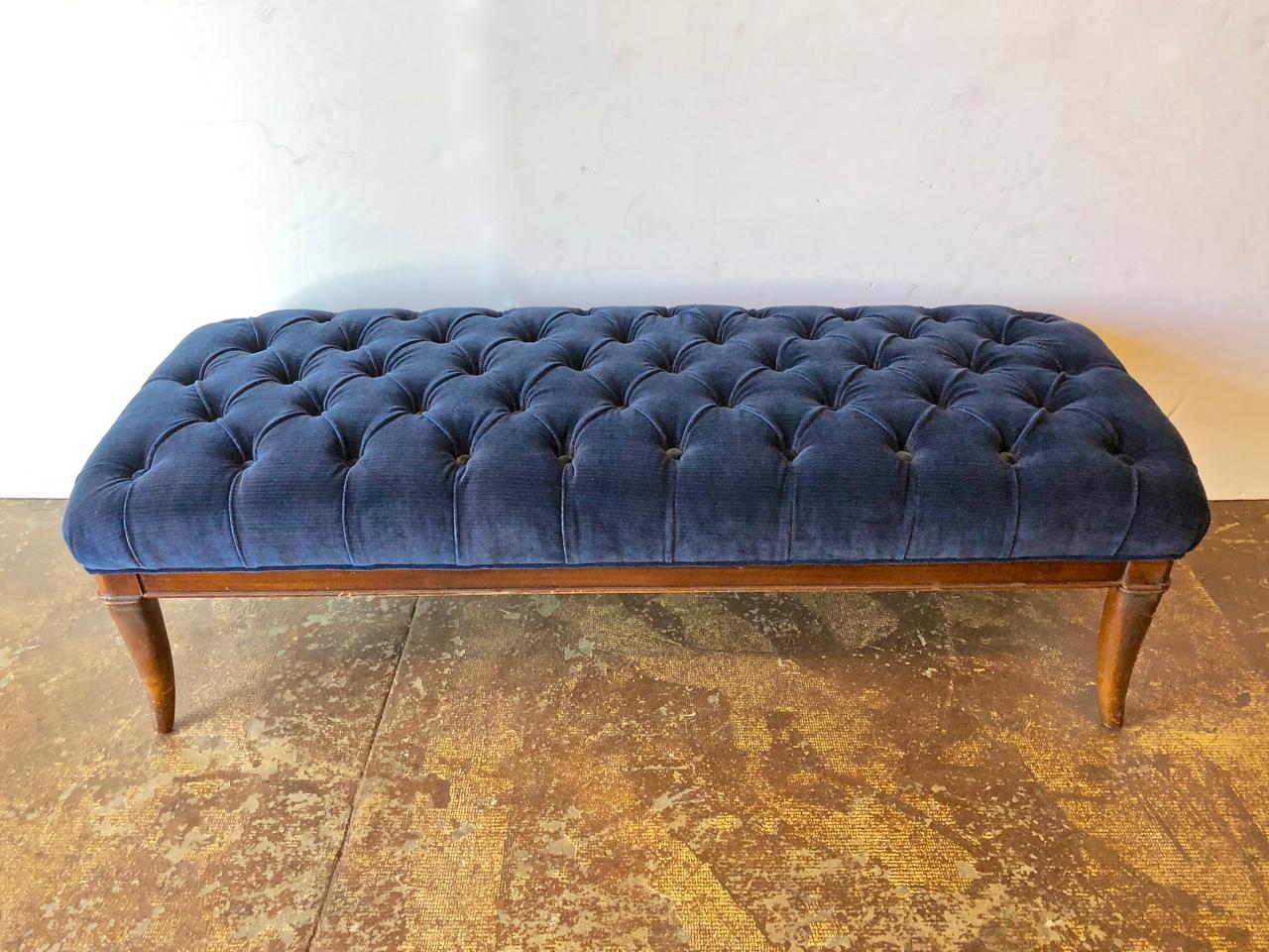 This is a chic midcentury bench in the style of Robsjohn-Gibbings that is. Newly upholstered in a rich blue Clarence House velvet. The tufting is of the highest level of craftsmanship, making this bench a stand out. The saber legs and generous