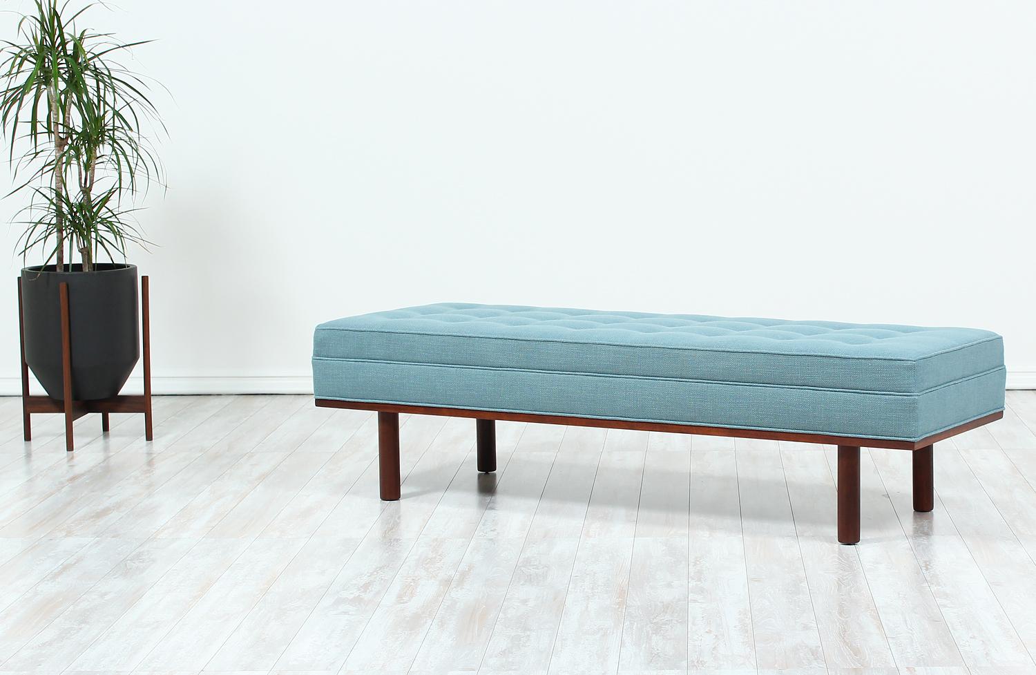 Mid-Century Modern bench designed and manufactured in the United States circa 1960s. This bench features a solid walnut wood base with cylindrical legs and a comfortable cushion with button-tufting detail. It has been re-upholstered with new