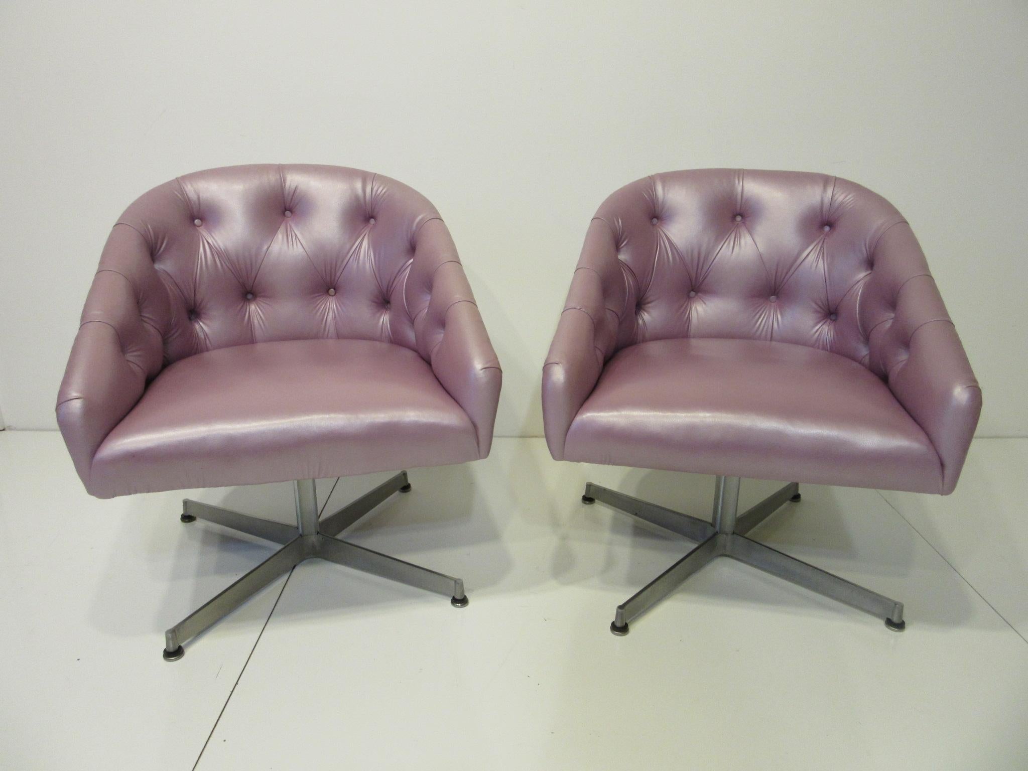 A pair of tufted chairs in a iridescent lavender original special order leatherette with cast aluminum swiveling star bases and domes of silent foot pads . Retains the original label to the bottom from the Shelby Williams Mfg. Company .