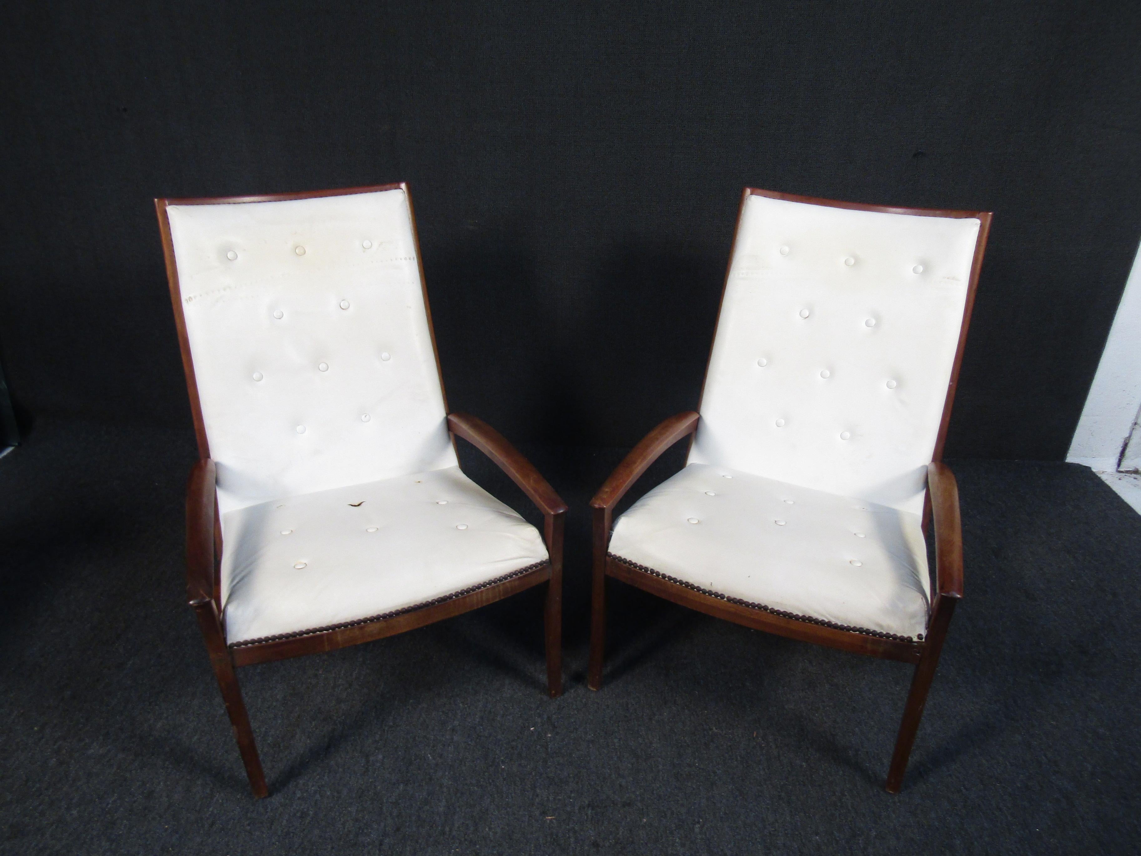 A classic pair of Mid-Century Modern lounge chairs. These chairs are a timeless design featuring tufted seats, sloped wooden arm rests and base, as well as white vinyl upholstered seats. A nice addition to any living room space.

Please confirm