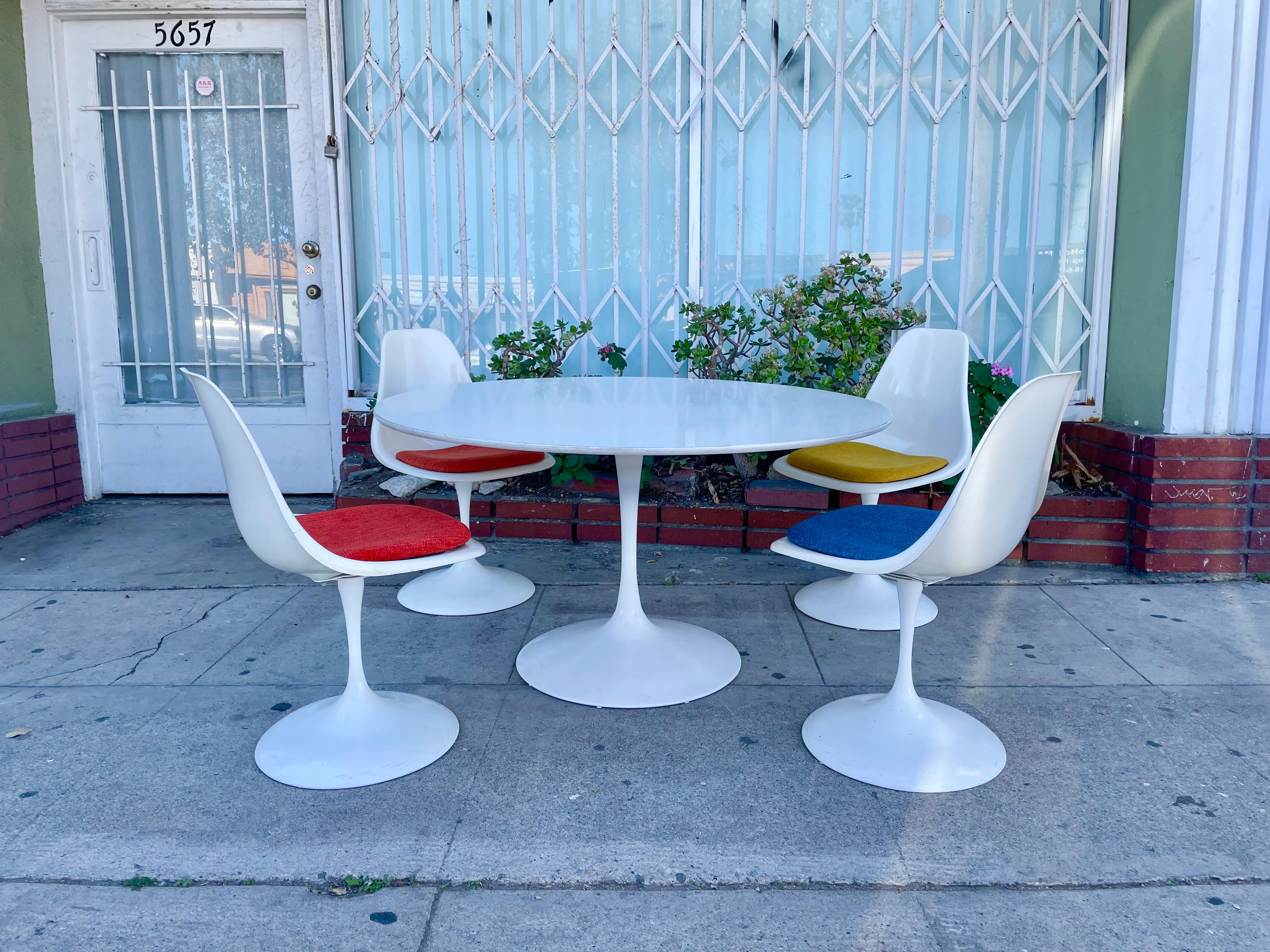 Midcentury tulip dining table styled after Eero Saarinen; This beautiful set is just so unique and amazing dining set. It features four armless swivel chairs that have a white lacquer finish. The table has a white wooden top and a cast iron metal